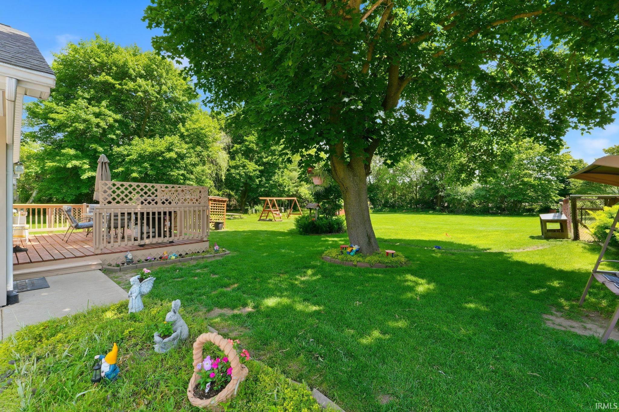 Expansive green lawn with mature trees and a wooden deck featuring lattice railing
