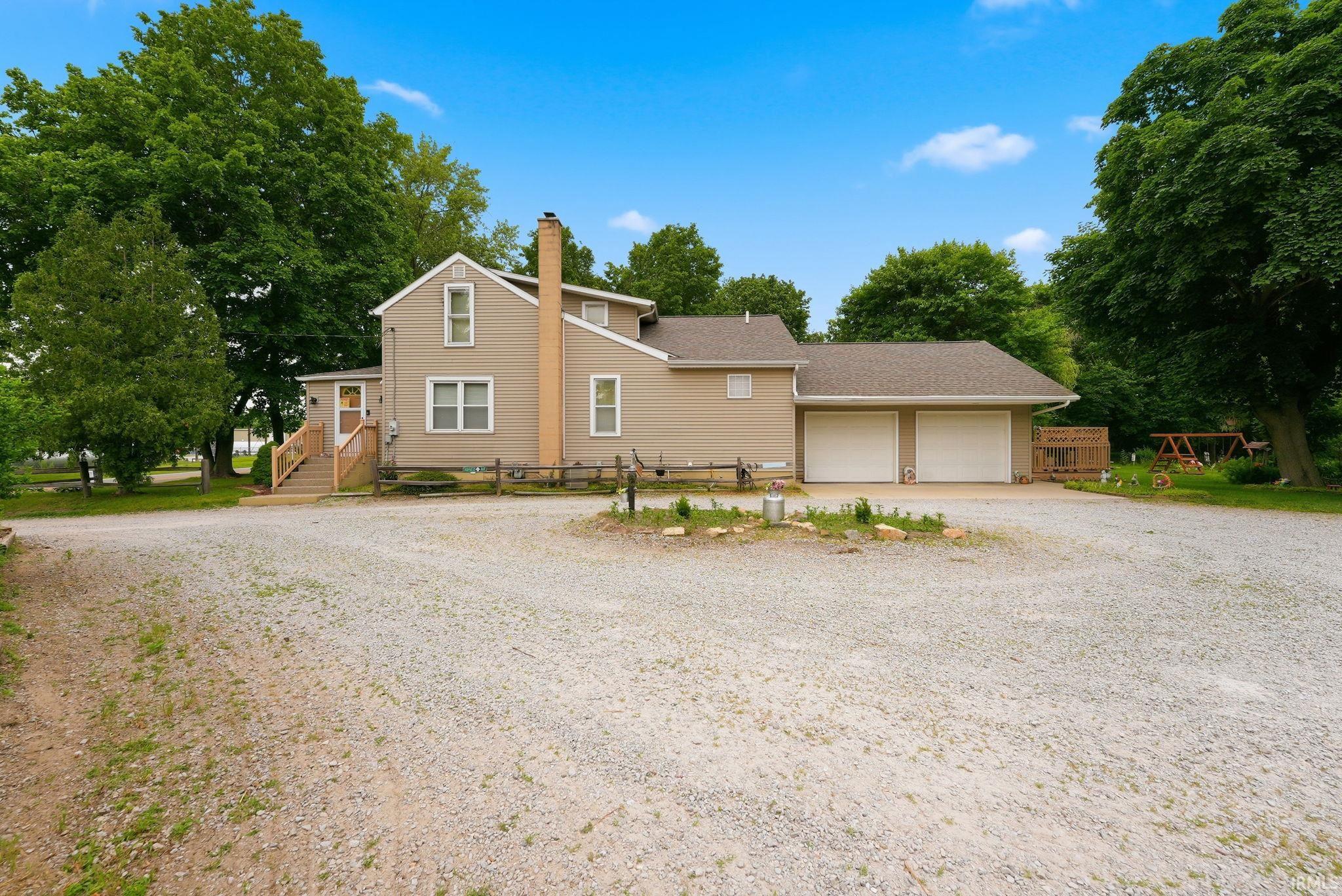 Two-story residence with neutral siding, a prominent brick chimney, and a gravel driveway