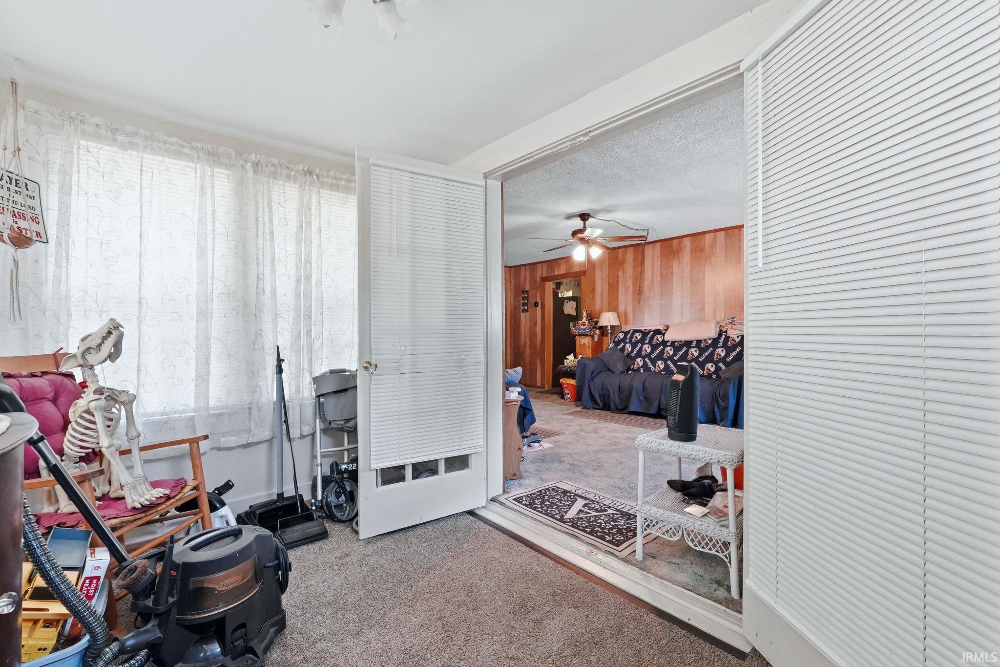 Carpeted sunroom with extensive window line, ceiling fan, and French doors opening to an interior room with wood-paneled walls