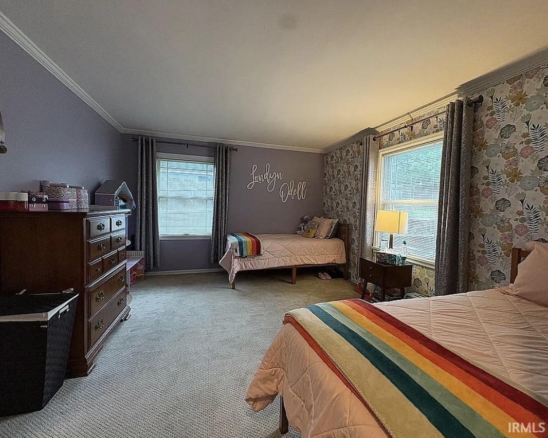 Spacious room featuring light gray carpeting, two large windows with gray curtains, white crown molding, and an accent wall with floral wallpaper
