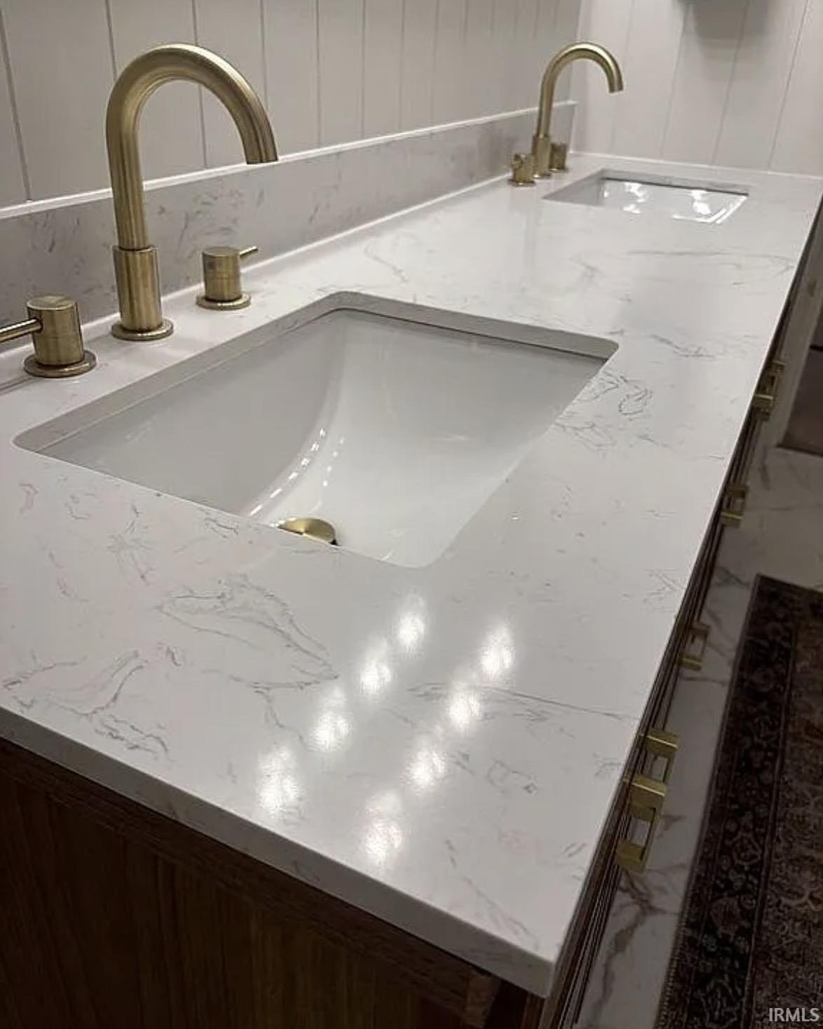 Dual vanity featuring an integrated sink with brushed brass fixtures, white veined countertop, and wood-finish cabinetry