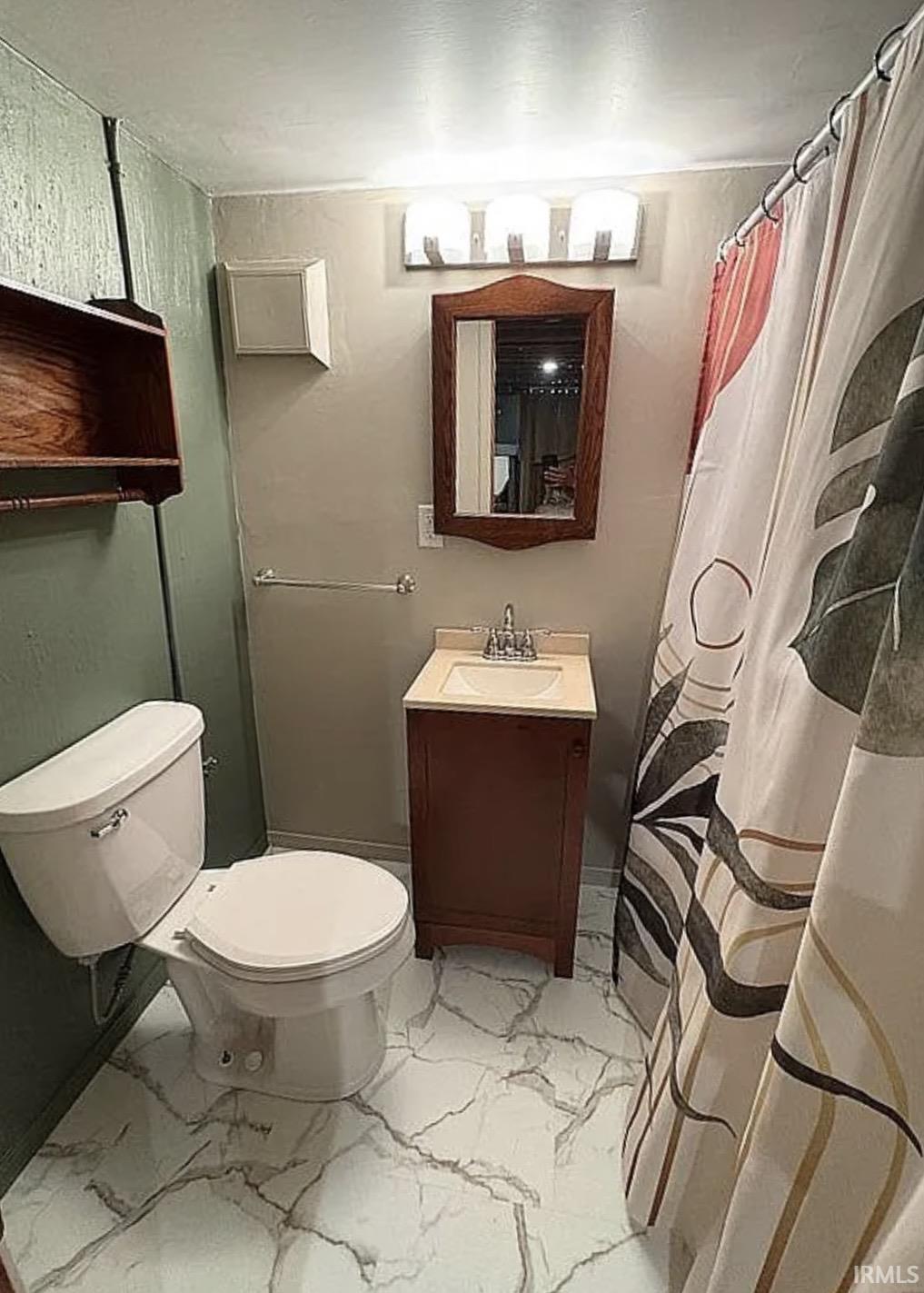 Contemporary bathroom featuring a white toilet, freestanding wood-finish vanity with an integrated sink, and a framed mirror
