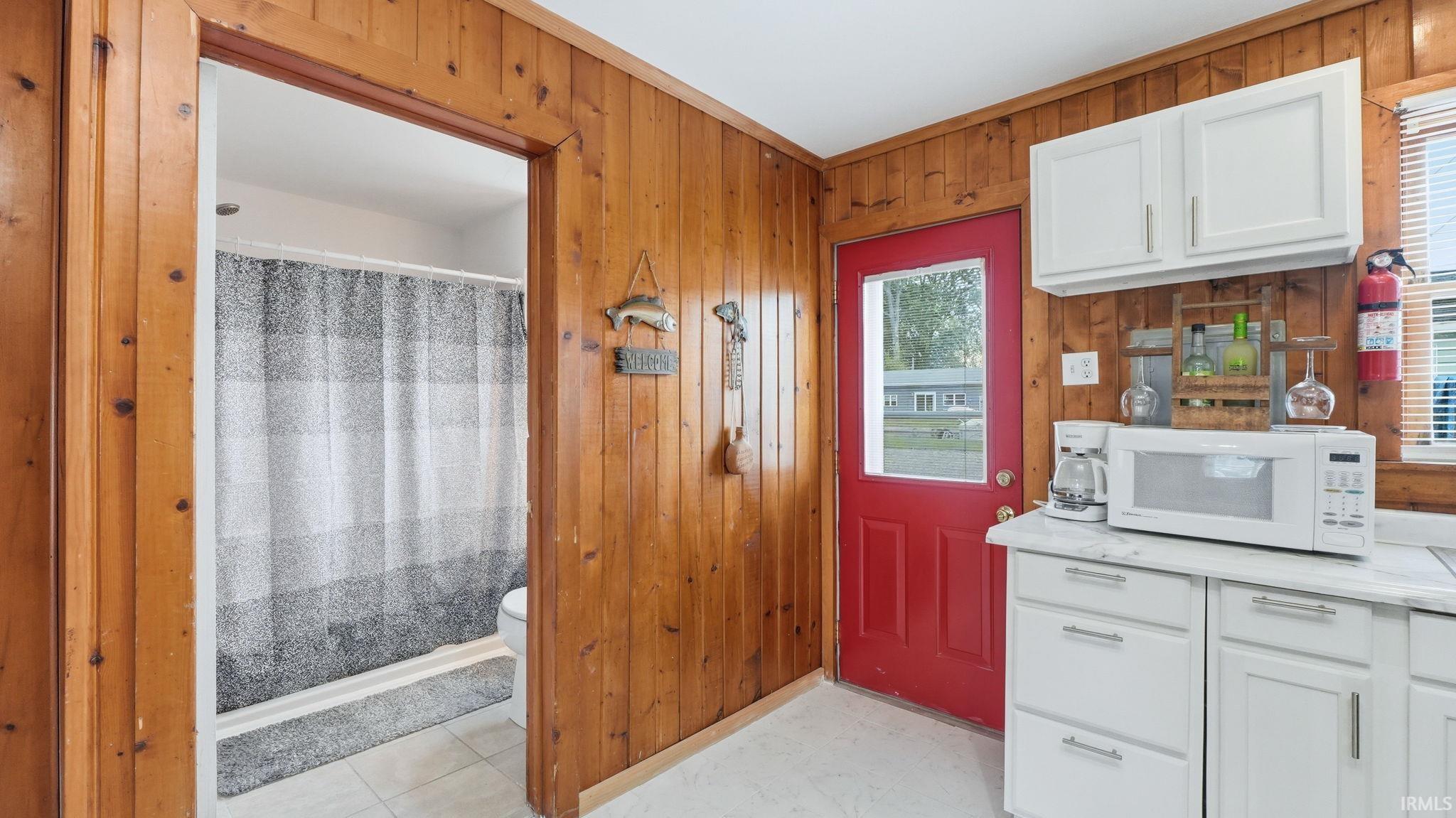 Kitchenette featuring white cabinetry, light-toned countertops, and a vibrant red entry door with a window pane