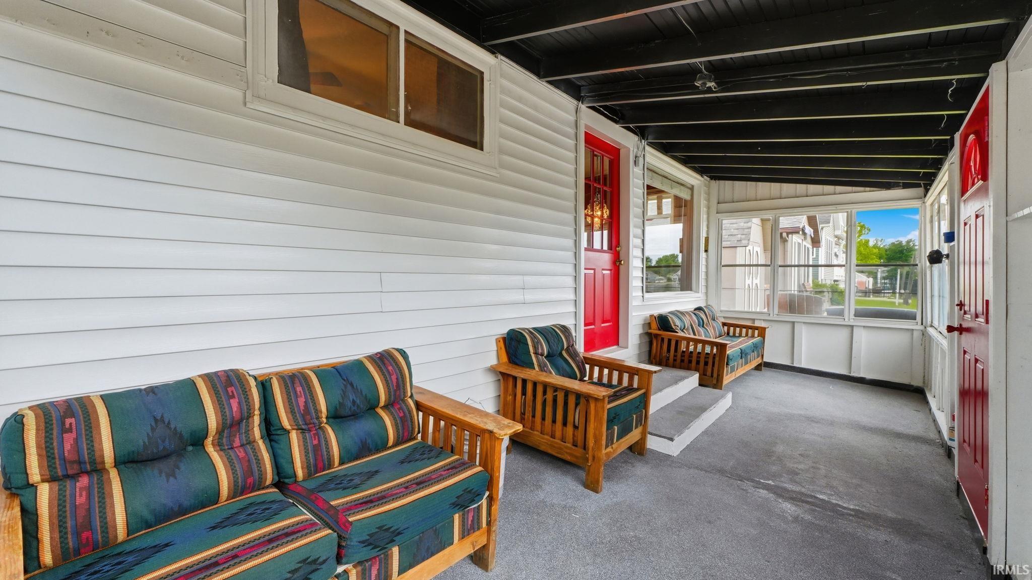 Enclosed porch featuring white vinyl siding, a red entry door, and a black exposed beam ceiling