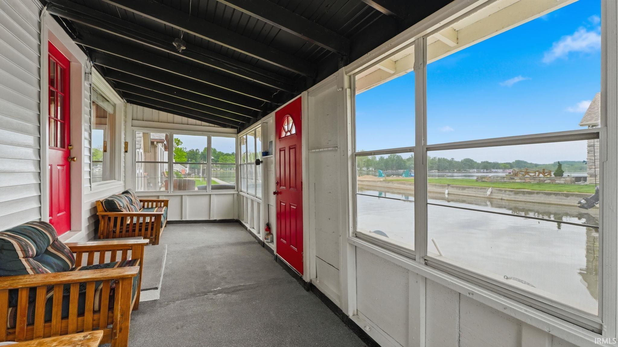 Enclosed porch with white siding walls, black ceiling rafters, and red doors