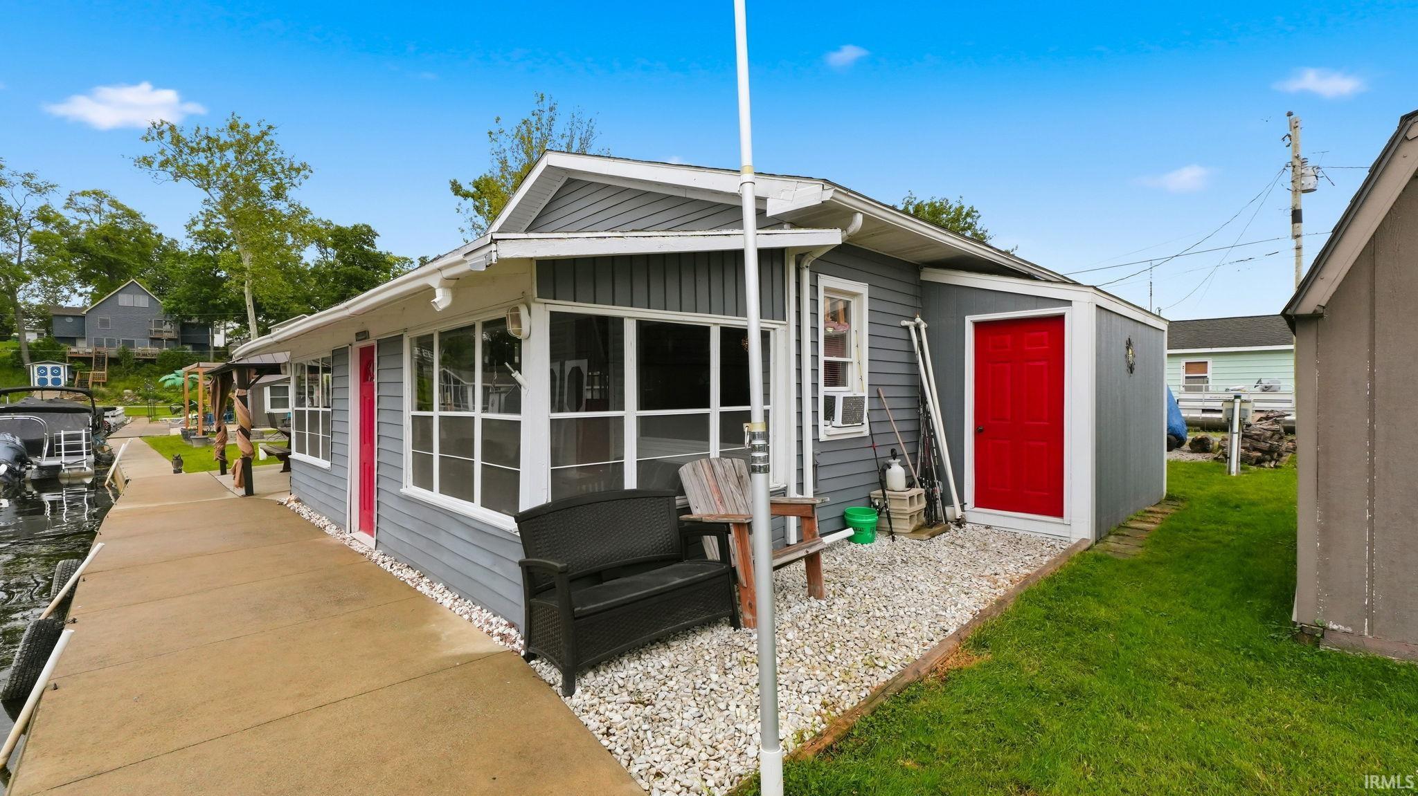 Waterfront property featuring a concrete dock, gray siding, white trim, and bright red entry doors