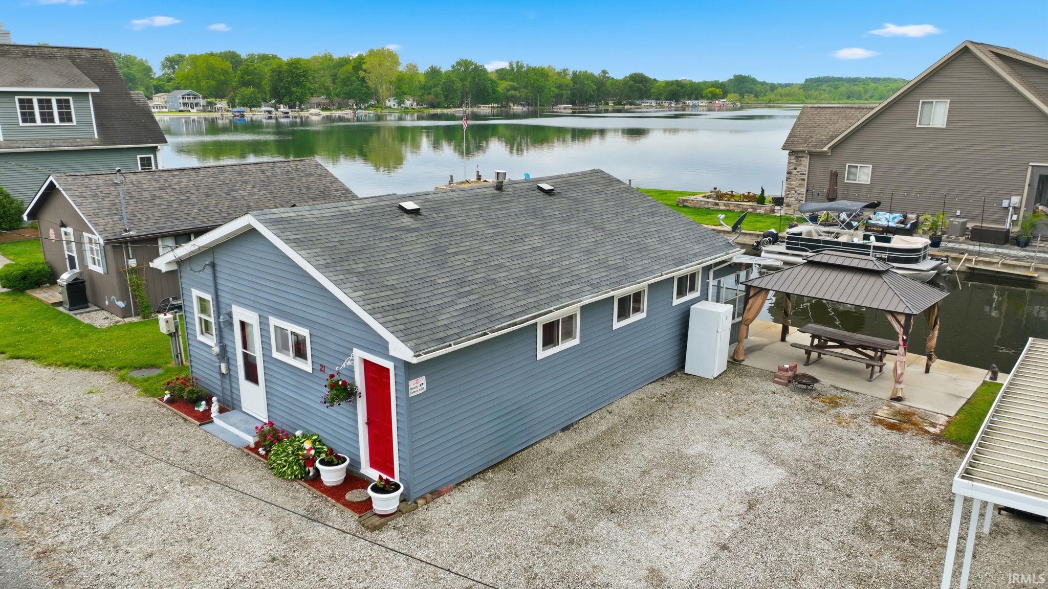 Waterfront property featuring a blue siding exterior, a red entry door, a private dock, and a covered outdoor entertaining area