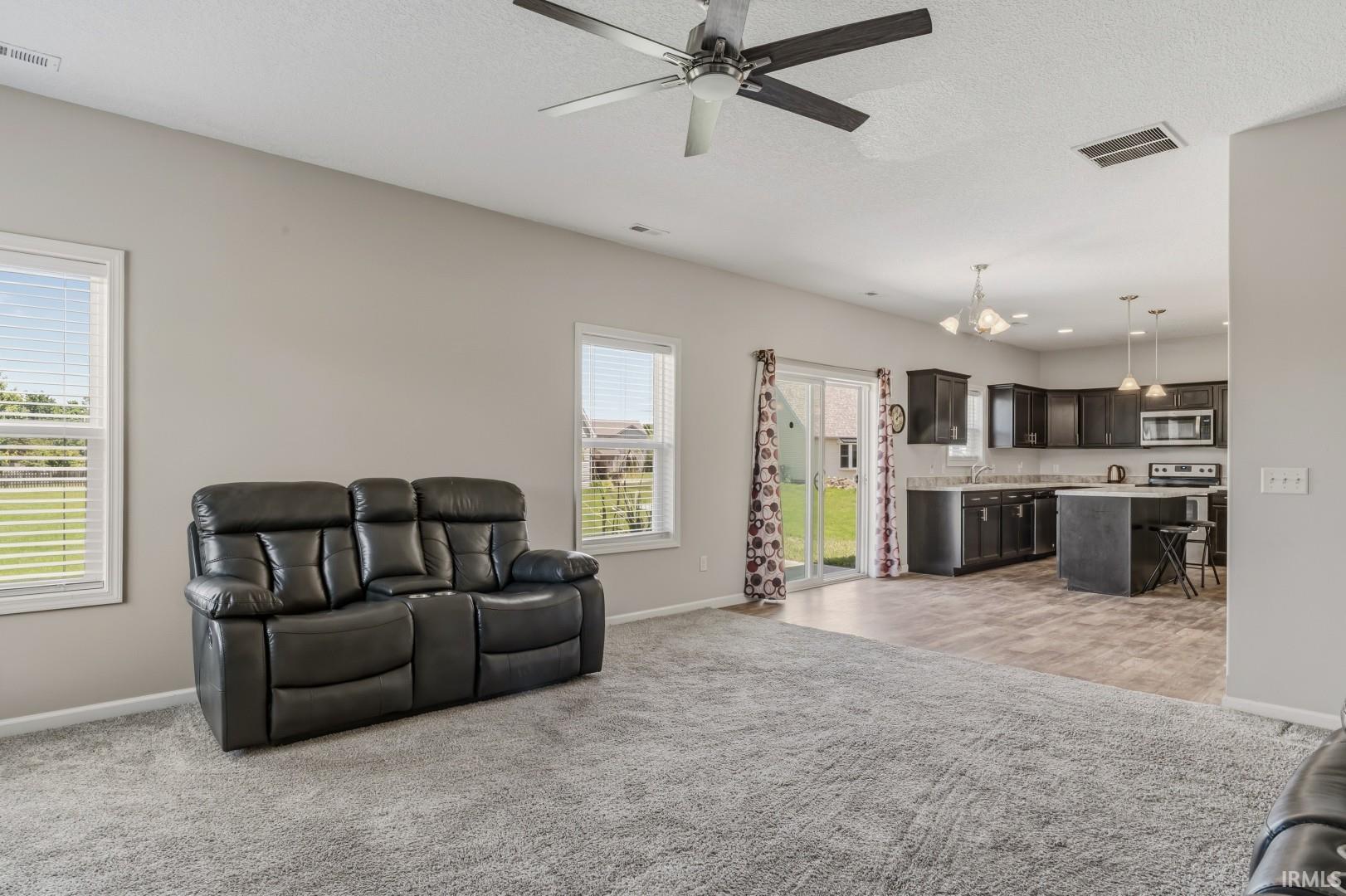 Open-concept living space featuring a ceiling fan, two windows with blinds, and light gray wall paint