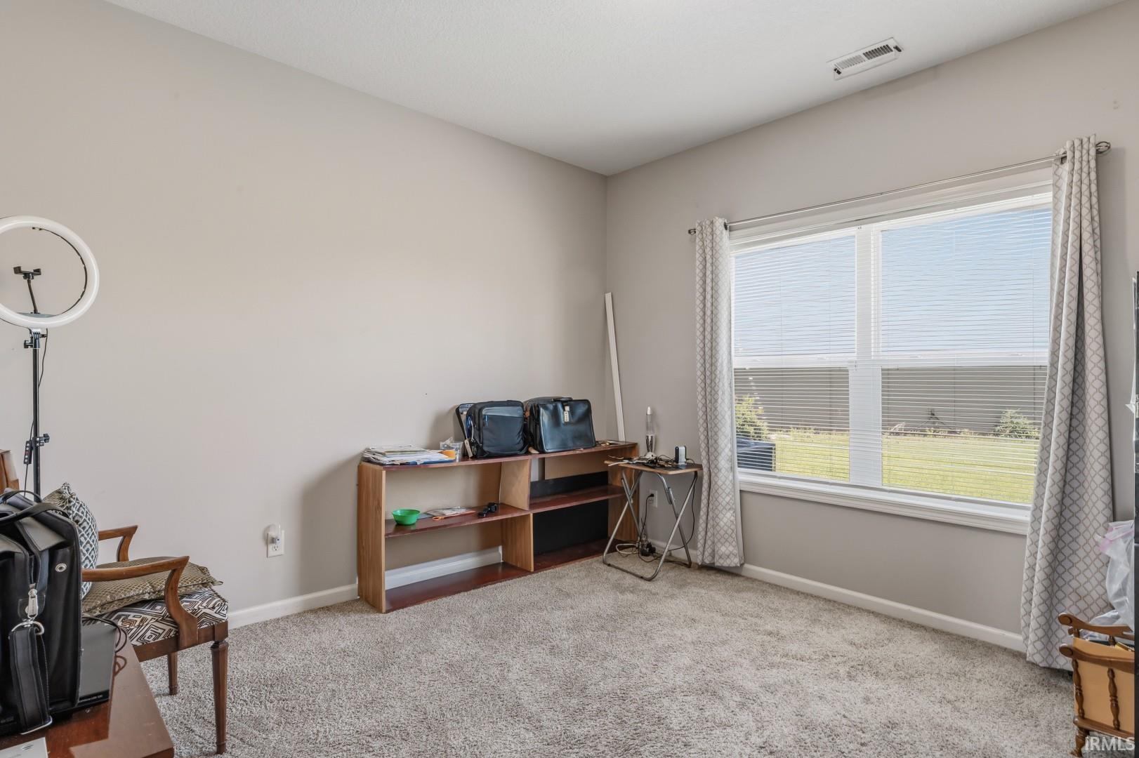 Carpeted interior space featuring a large window with blinds, light gray walls, and a white ceiling