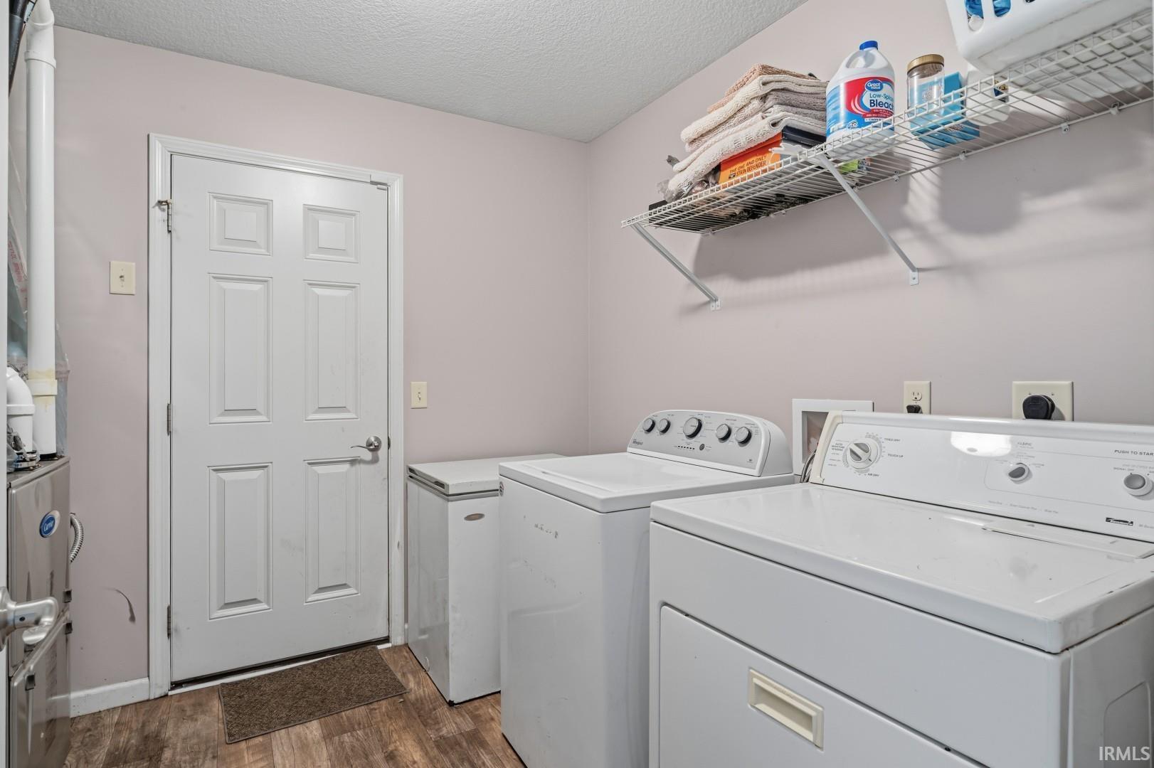 Utility room featuring wood-finish flooring, a white paneled door, and a wall-mounted wire shelving unit