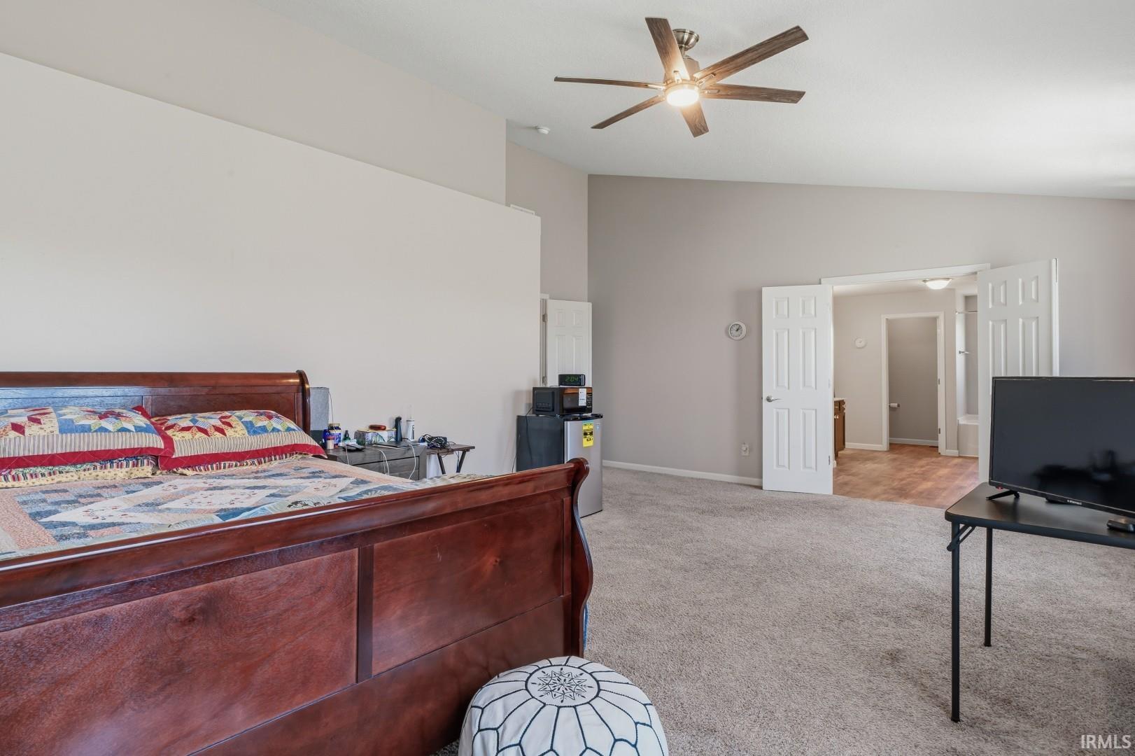 Spacious carpeted room featuring vaulted ceilings, a ceiling fan with integrated lighting, and neutral wall tones