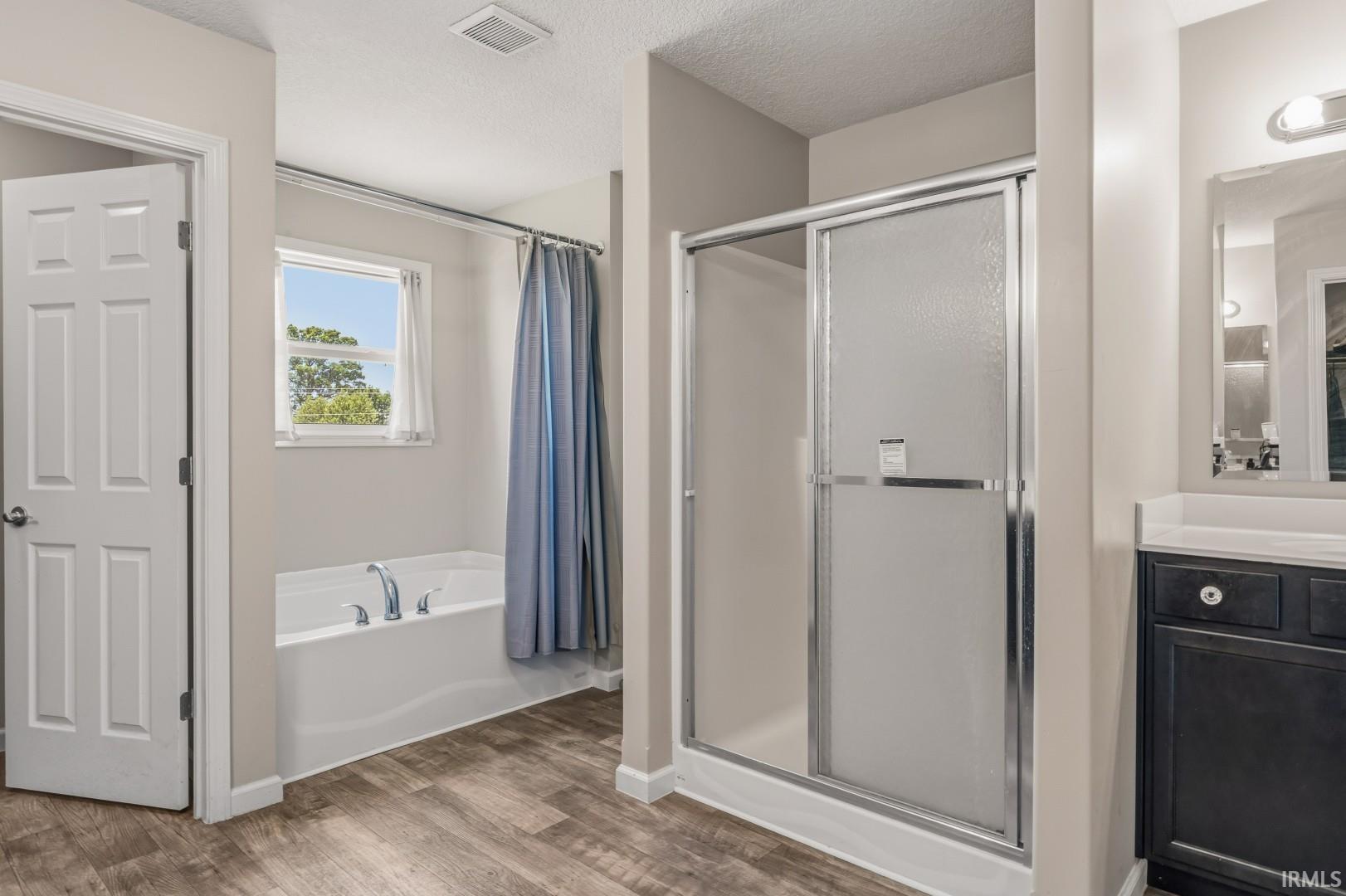 Bathroom featuring a white built-in tub, a shower with a sliding frosted glass door, a dark wood-finish vanity with a white countertop, chrome fixtures, and wood-finish flooring