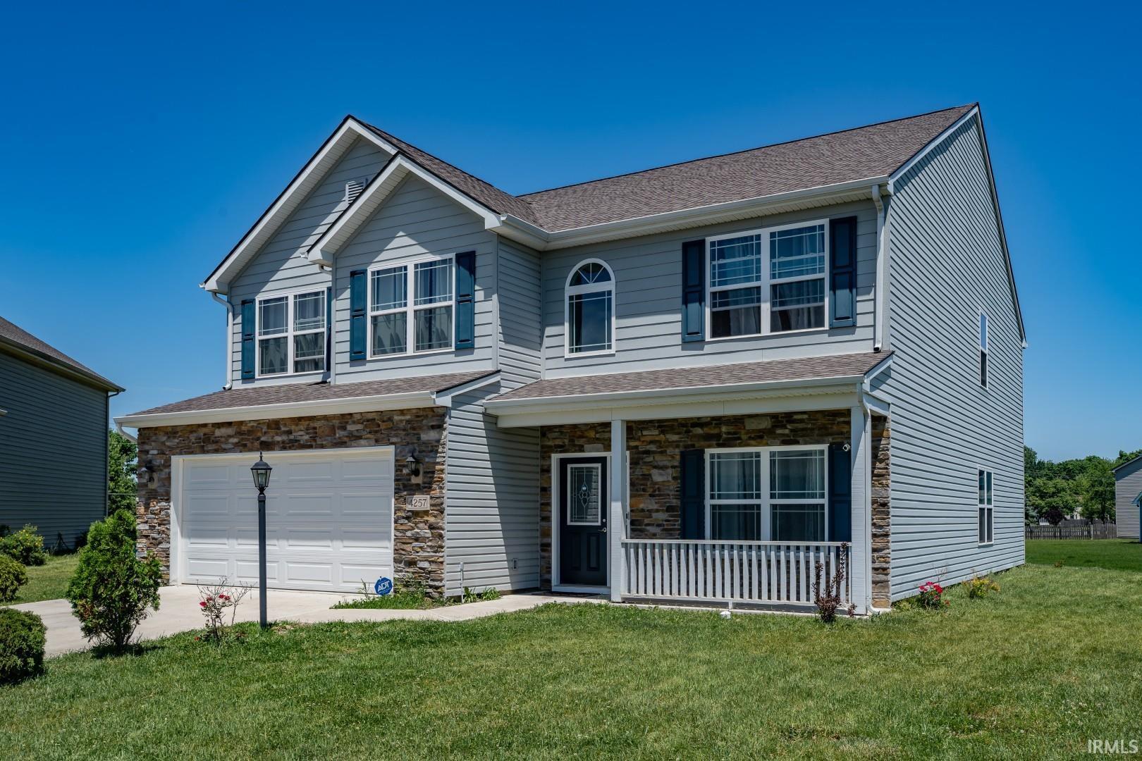 Two-story residential property featuring a light blue siding exterior with stone accenting, a two-car garage, and a covered front porch with white railing