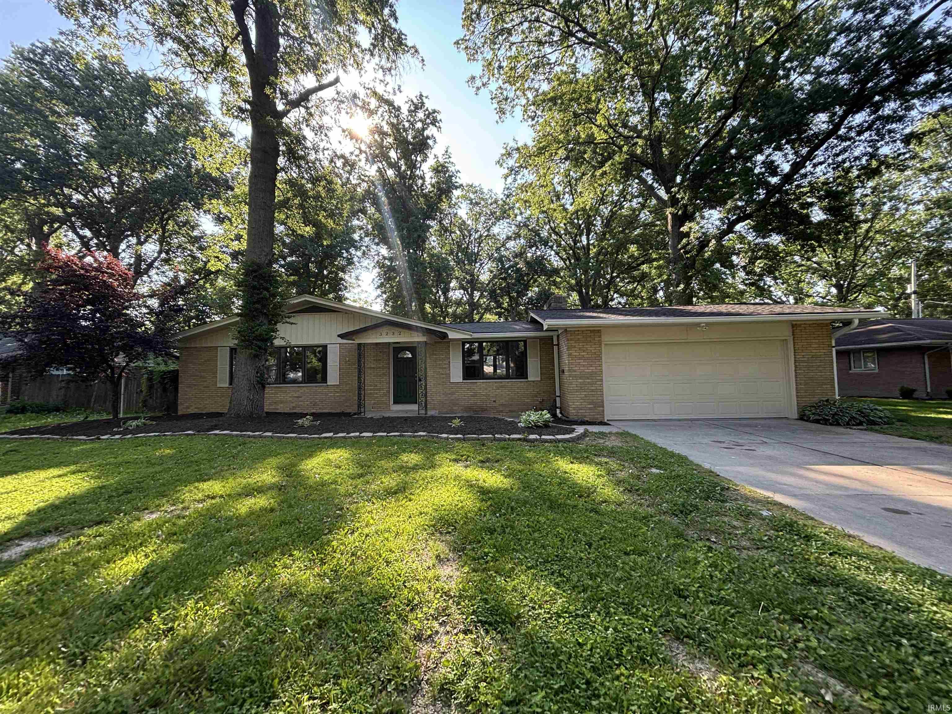 Ranch-style exterior featuring brick facade, a two-car garage, and established landscaping
