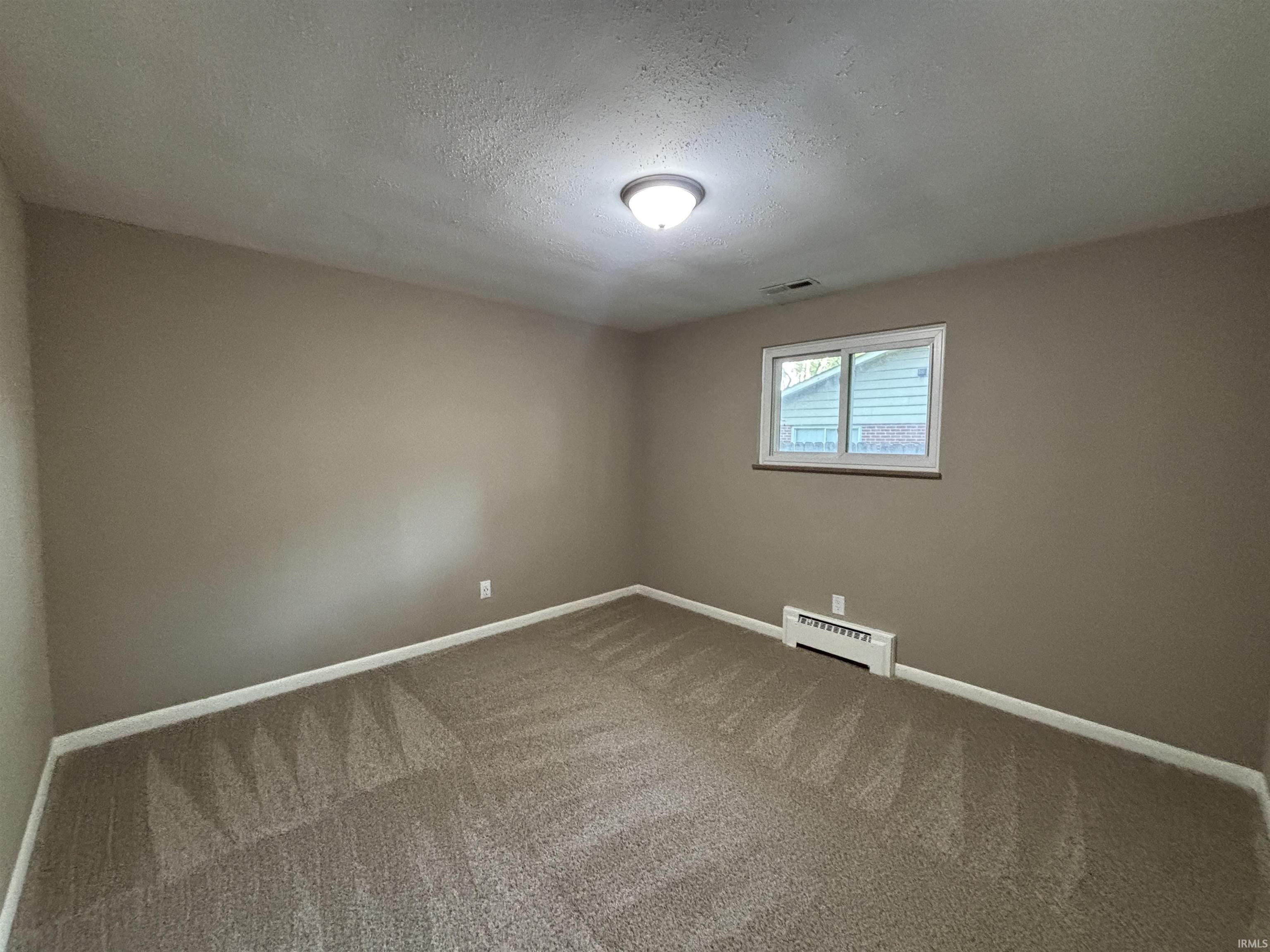 Room featuring light tan walls, a white ceiling with a flush-mount light fixture, and patterned carpet flooring