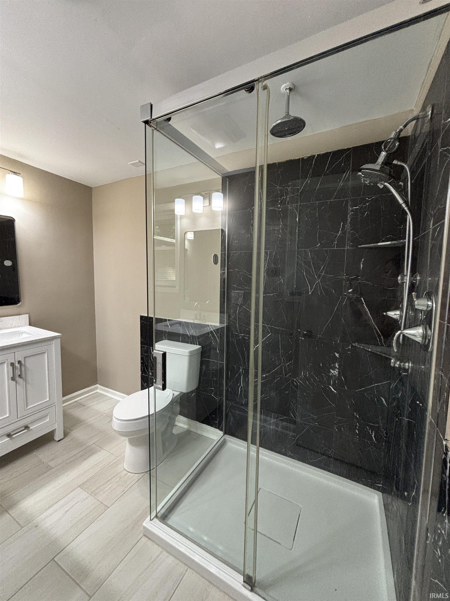 Enclosed glass shower featuring dark-toned marble-look tile, rainfall showerhead, and a multi-function shower system