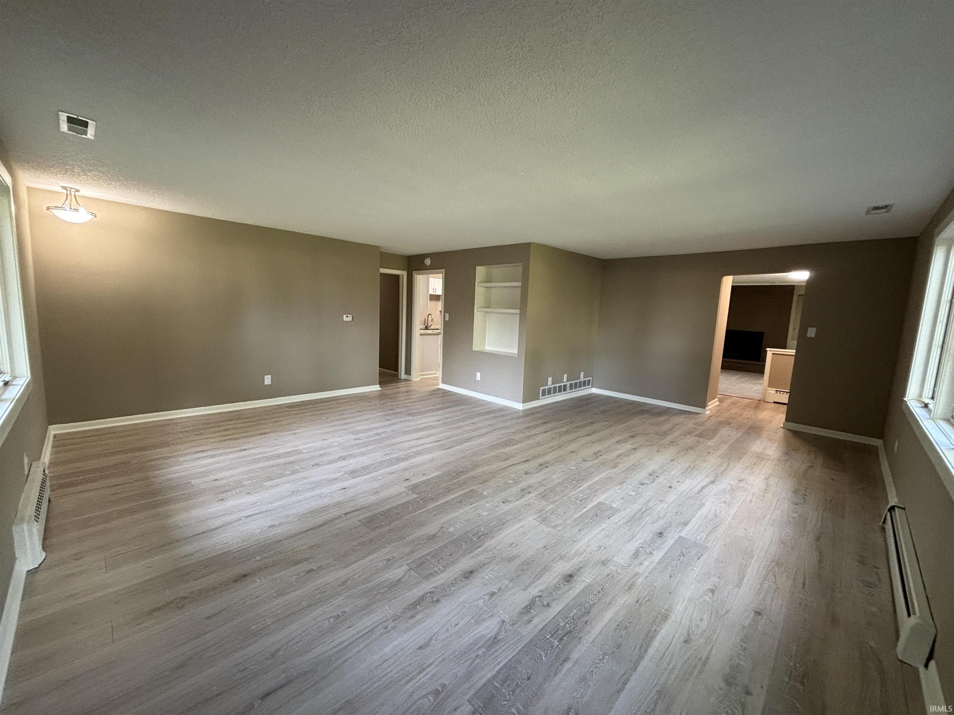 Spacious interior featuring wood-finish flooring, neutral wall tones, white baseboards, and built-in shelving