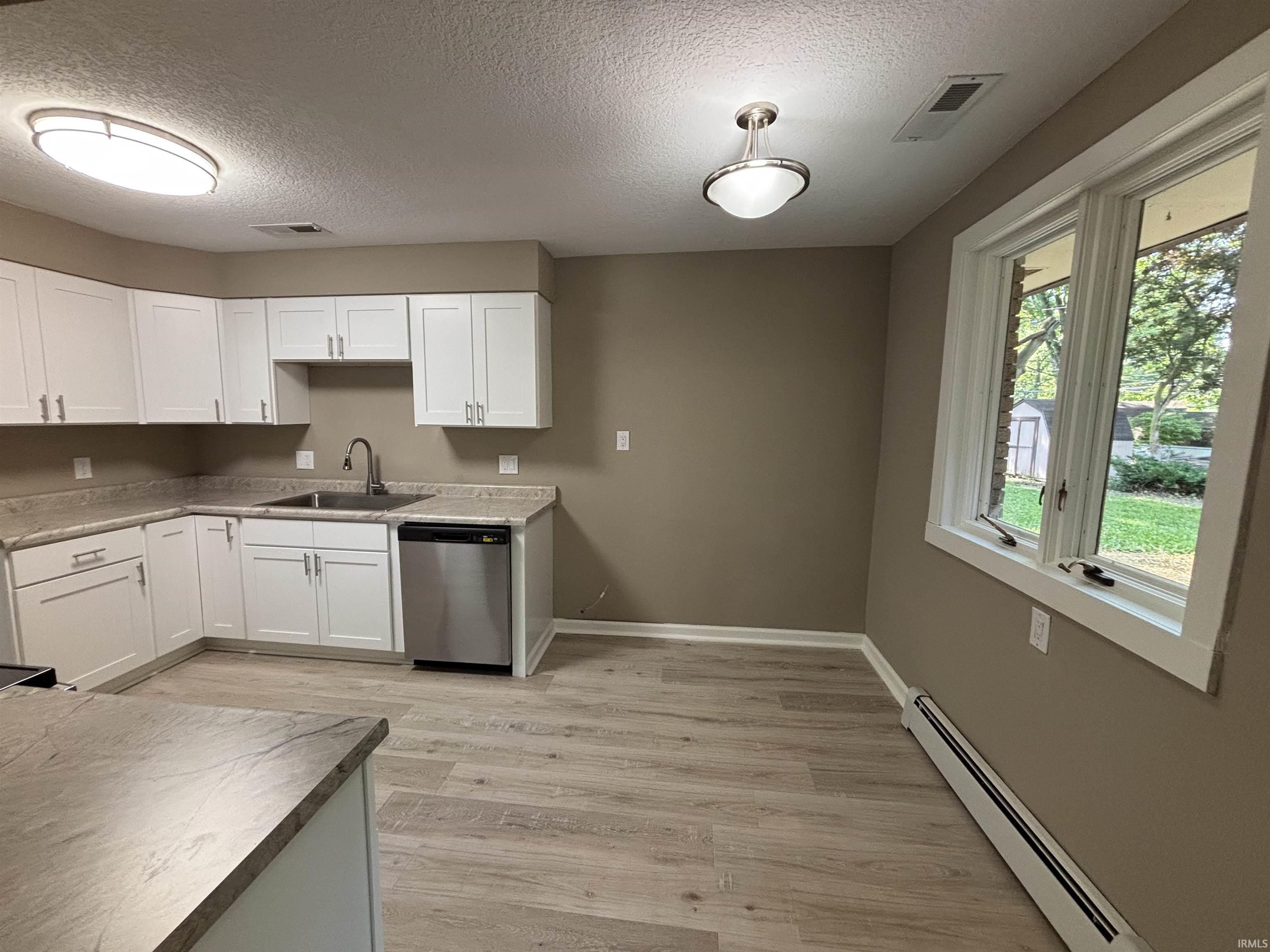 Kitchen featuring L-shaped white cabinetry, stainless steel dishwasher, light-toned countertops, and wood-finish flooring