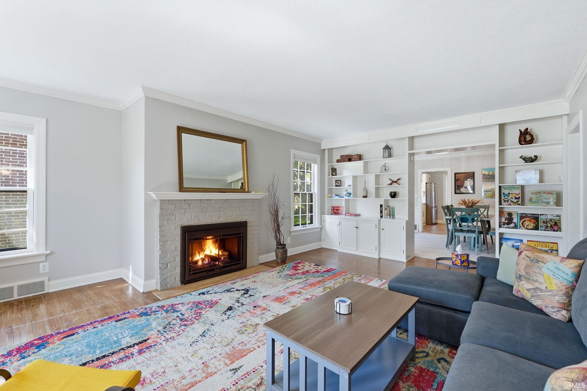 Living area featuring a painted brick fireplace with a mantel, built-in shelving, wood-finish flooring, and white trim