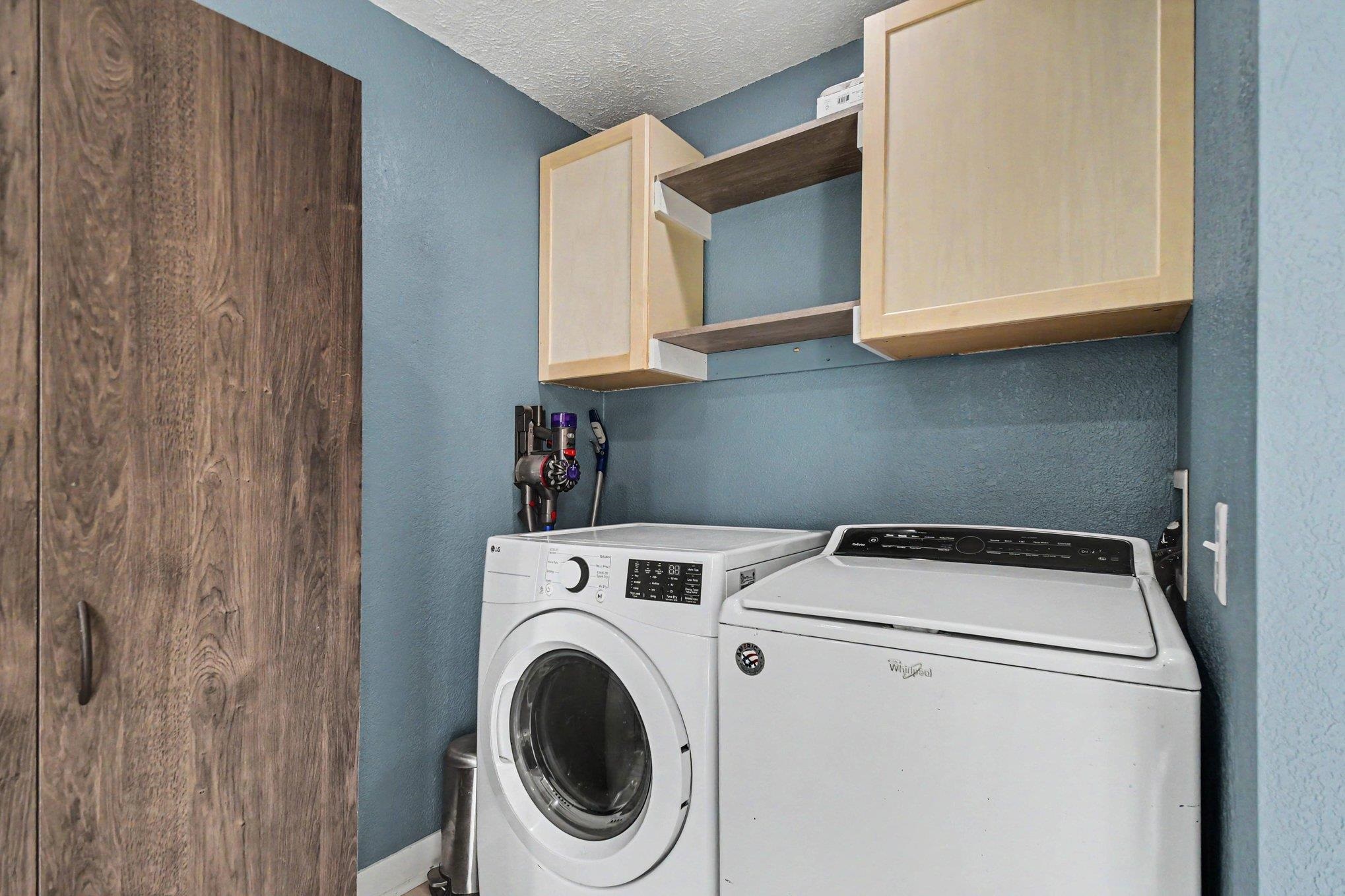 Laundry area featuring blue walls, wood-finish storage cabinetry, light wood-finish upper cabinets, and open shelving