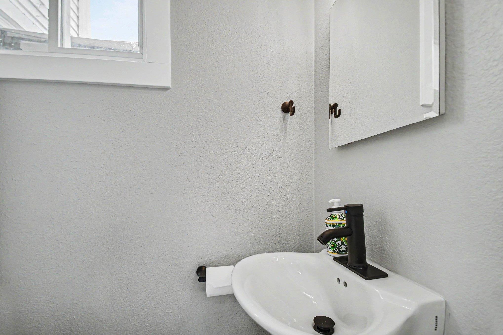 Pedestal-style sink with a dark bronze faucet, wall-mounted mirror, and a window with white trim
