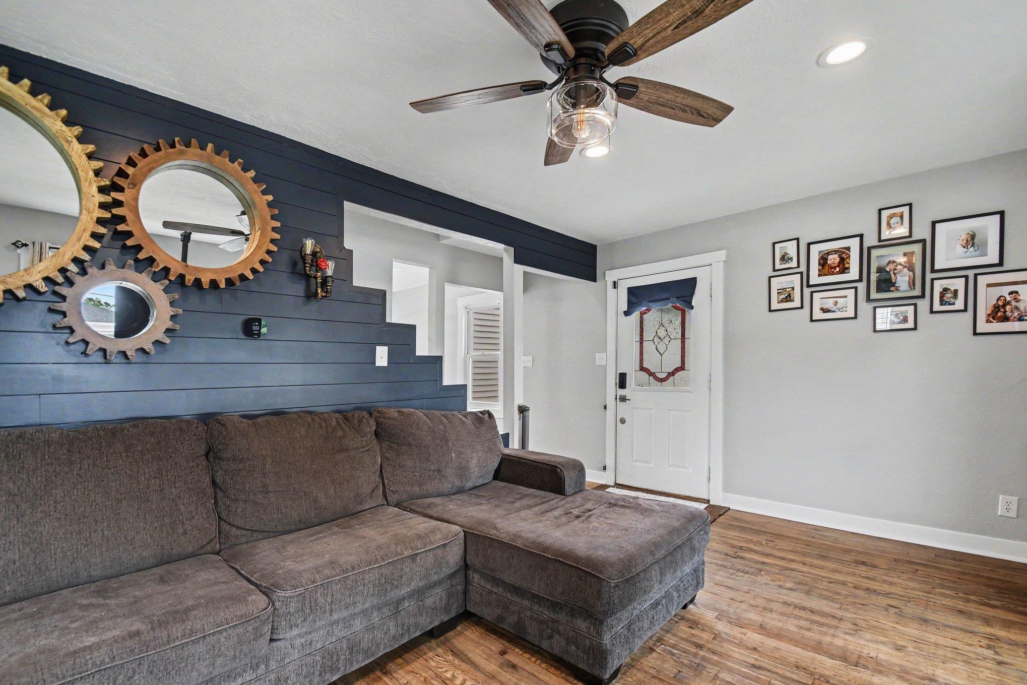 Living area featuring wood-finish flooring, a ceiling fan with light fixture, recessed lighting, a white entry door with decorative glass, and a shiplap accent wall