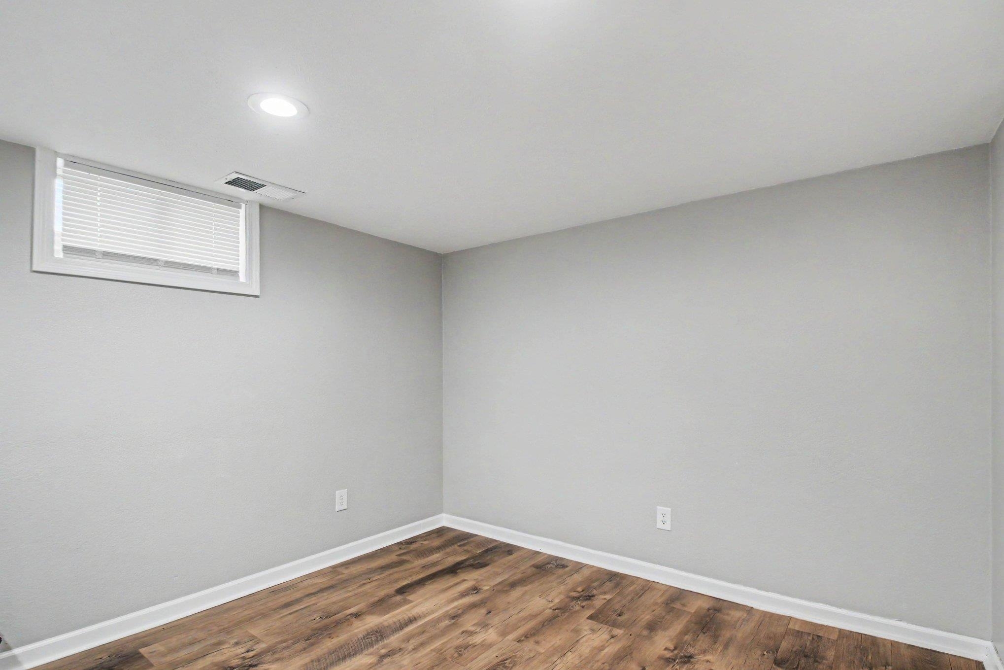 Spacious room featuring wood-finish flooring, light gray wall paint, crisp white baseboards, and a recessed ceiling light