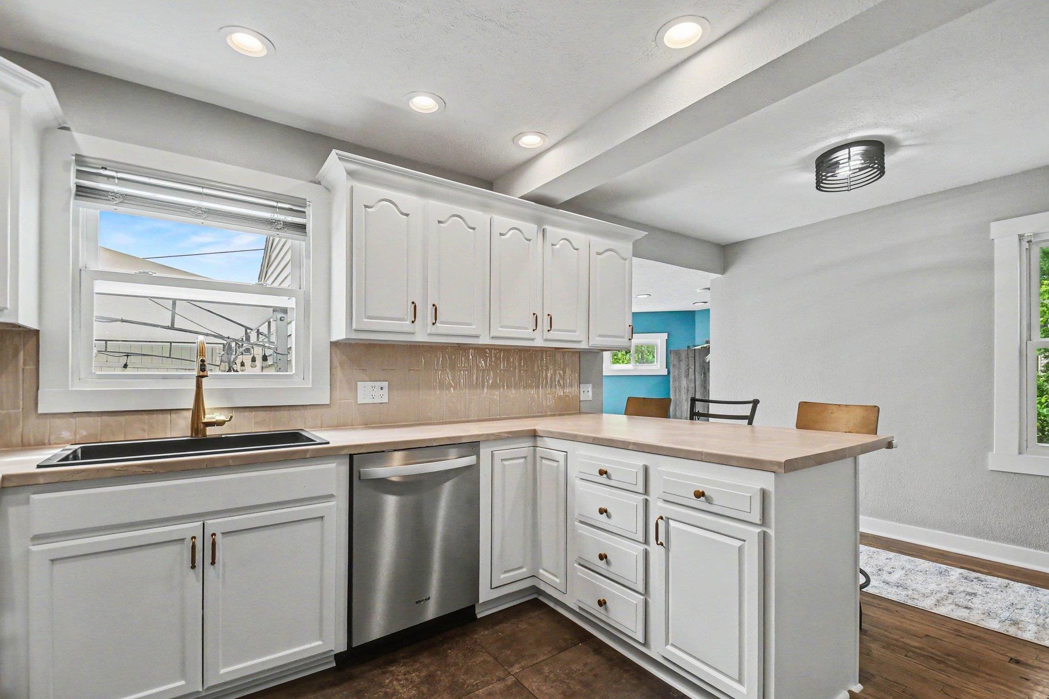 Kitchen featuring white cabinetry, a stainless steel dishwasher, an undermount sink with a brass-finish faucet, recessed lighting, and a neutral-toned backsplash