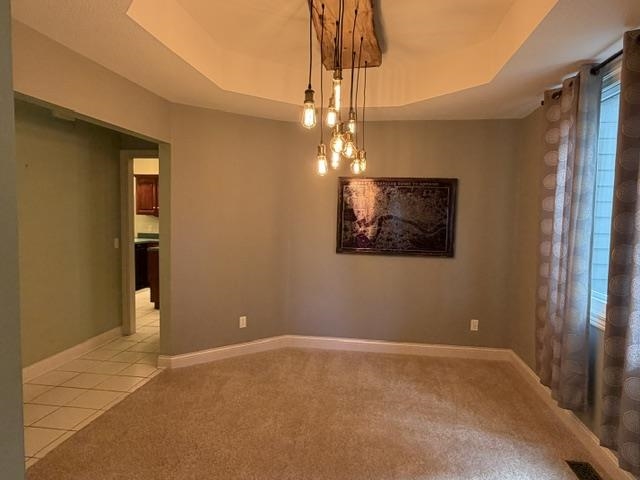 Tray ceiling with a multi-bulb industrial-style chandelier, carpeted flooring, and a window with installed curtain rod