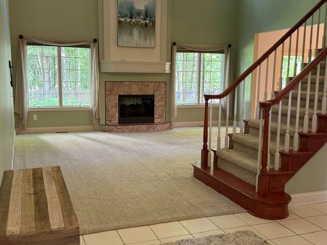 Living space featuring a corner fireplace with stone-look tile surround and mantle, high ceilings, multiple windows, and a hardwood staircase with white balusters