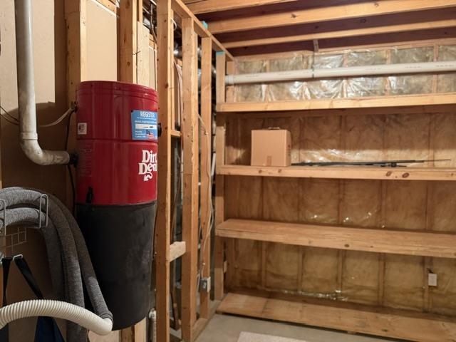 Utility area featuring a central vacuum system, exposed wood framing, and built-in wood shelving with insulation