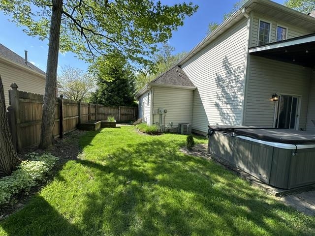 Fenced backyard featuring a built-in spa, wood fence, patio pavers, and mature trees