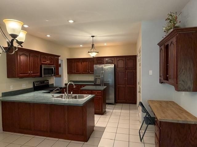 Kitchen featuring extensive wood cabinetry, an integrated kitchen island with a double basin sink, stainless steel appliances, and tile flooring