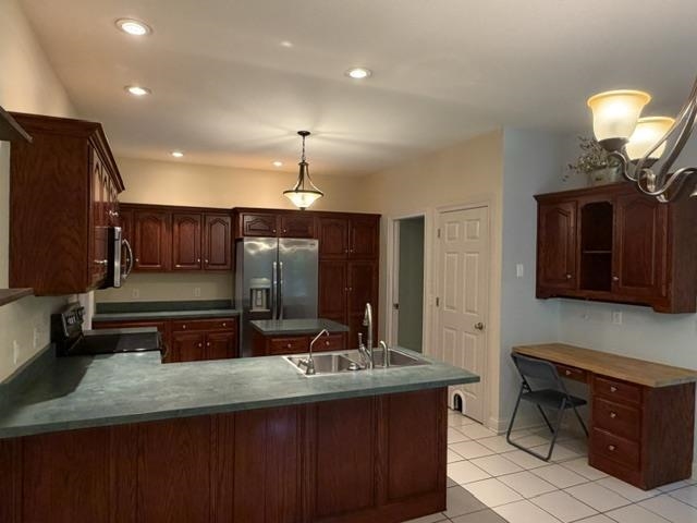 Kitchen featuring dark wood cabinetry, a stainless steel refrigerator, and a kitchen island with an integrated sink
