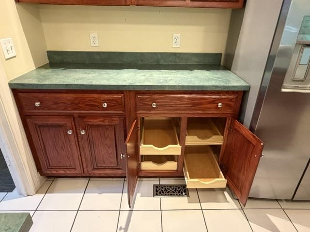 Rich wood-finish cabinetry with polished silver-tone hardware, green countertop, and white square tile flooring