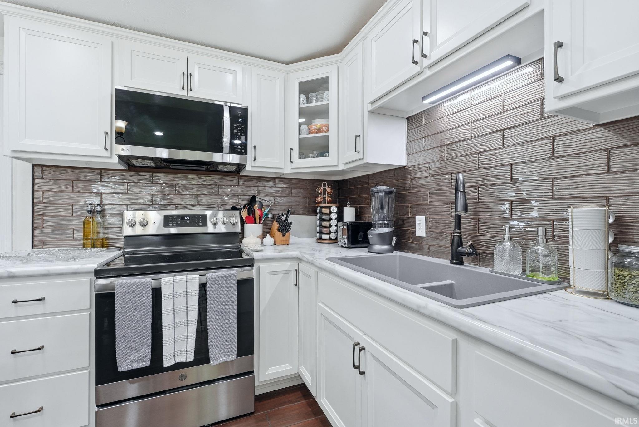 Modern kitchen featuring white shaker cabinetry, stainless steel appliances, a textured tile backsplash, a double basin sink with a matte black faucet, and stone-finish countertops