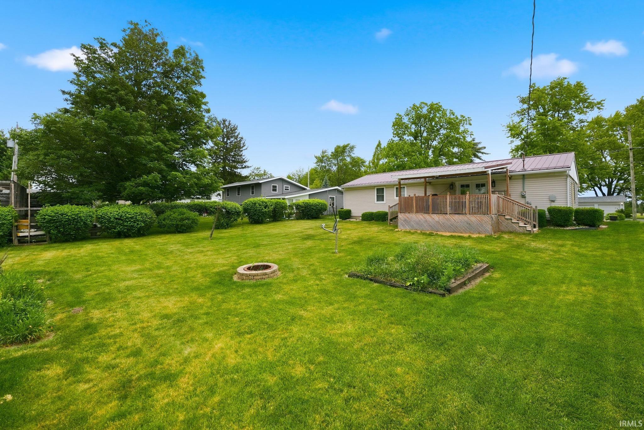 Expansive backyard featuring a large lawn, mature trees, a raised garden bed, and a stone fire pit