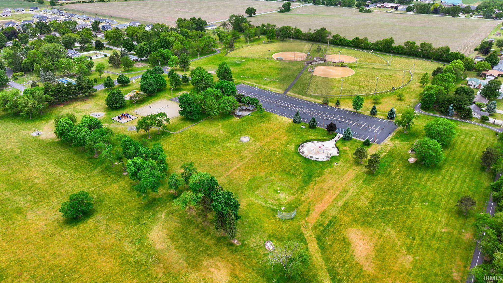 Expansive green spaces featuring multiple baseball fields, a large asphalt parking area, and a distinct circular paved area