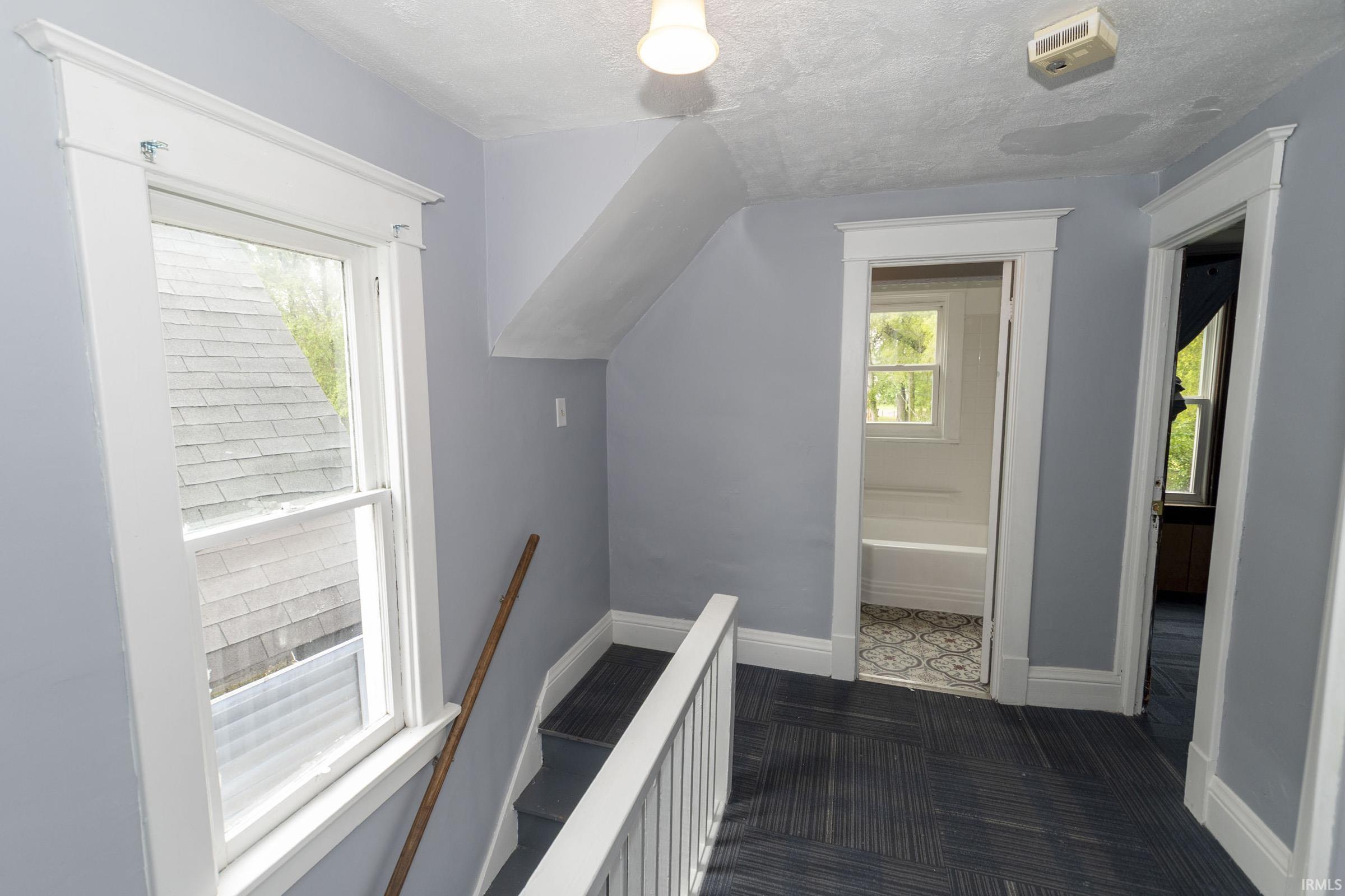 Upper-level landing featuring a single-hung window with white trim, a painted banister, and patterned carpet flooring