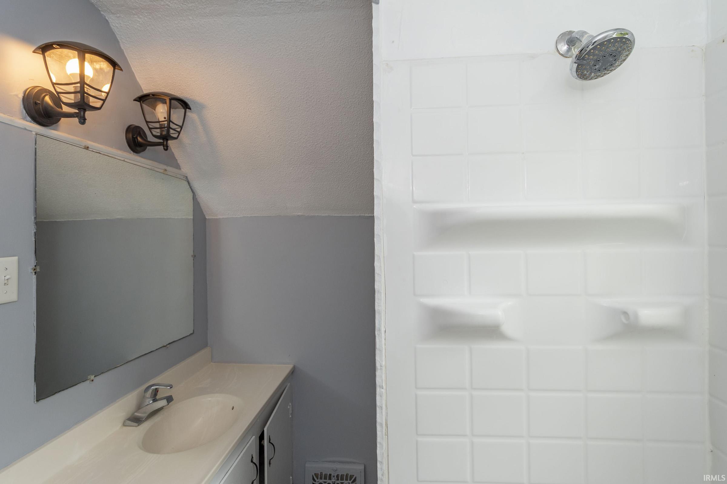 Bathroom vanity featuring a single basin, wall-mounted mirror, and overhead sconce lighting