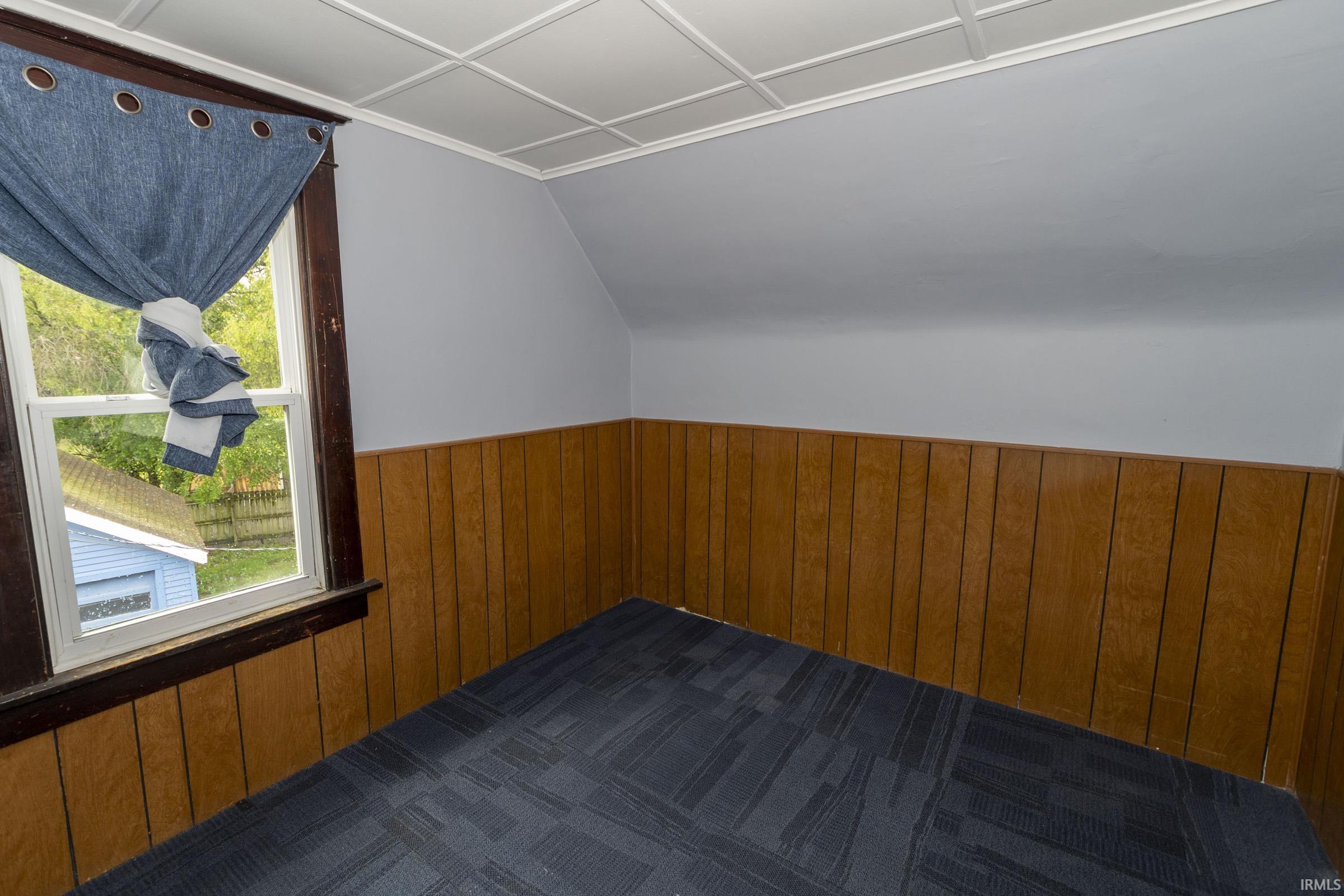 Interior room featuring a sloped ceiling, light blue painted walls, wood-finish paneling, and a white grid-patterned ceiling