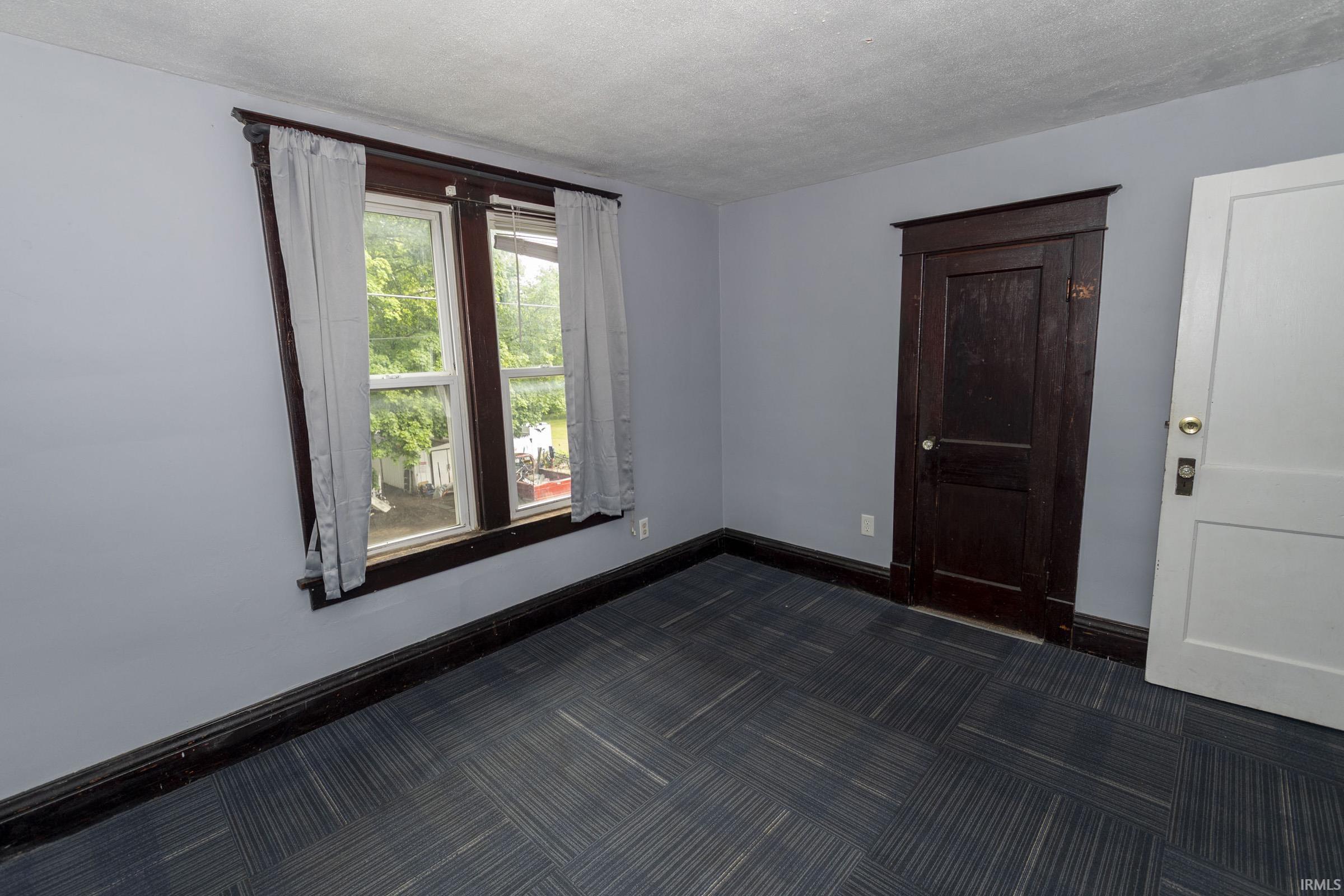 Room featuring light blue walls, dark wood trim, a window with white sashes, and patterned carpet flooring