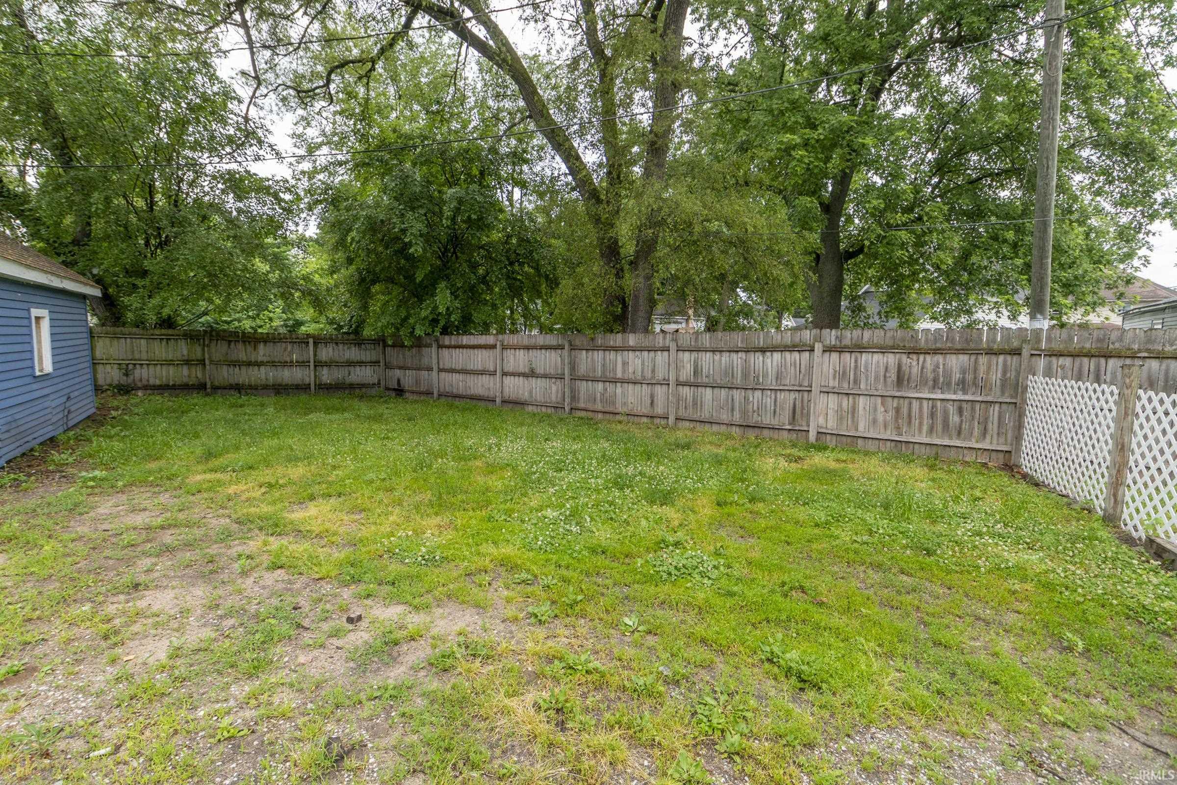 Expansive outdoor space featuring a wood privacy fence, partial white lattice fence, and mature trees providing a natural canopy