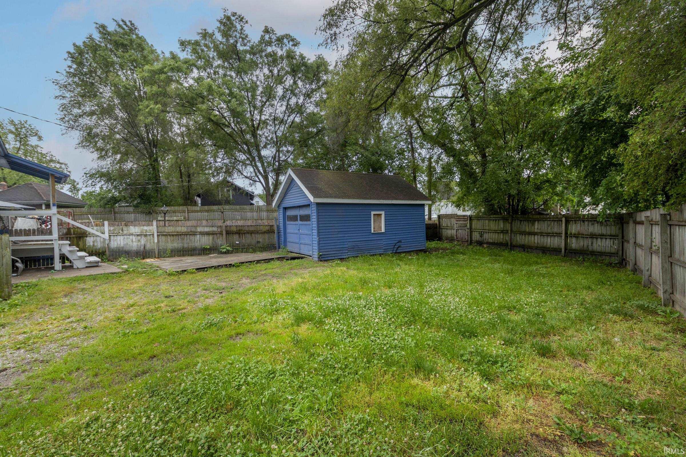 Spacious backyard featuring a detached garage with blue siding, wood fencing, a verdant lawn, and mature trees