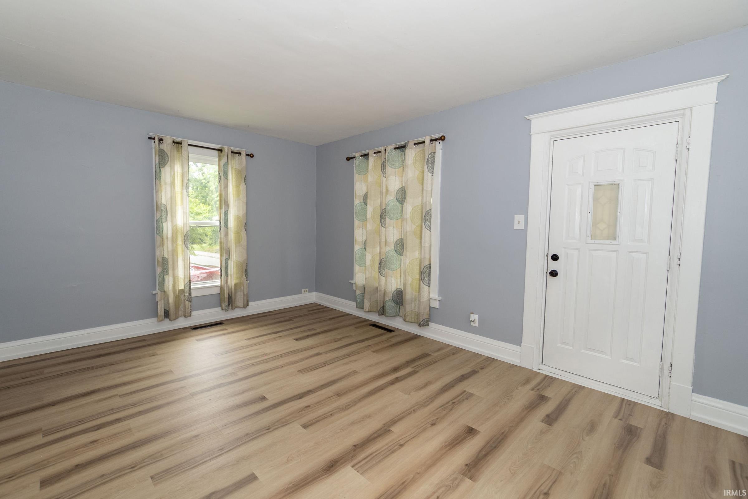 Entryway featuring wood-finish flooring, two window openings, and a paneled door with decorative glass insert