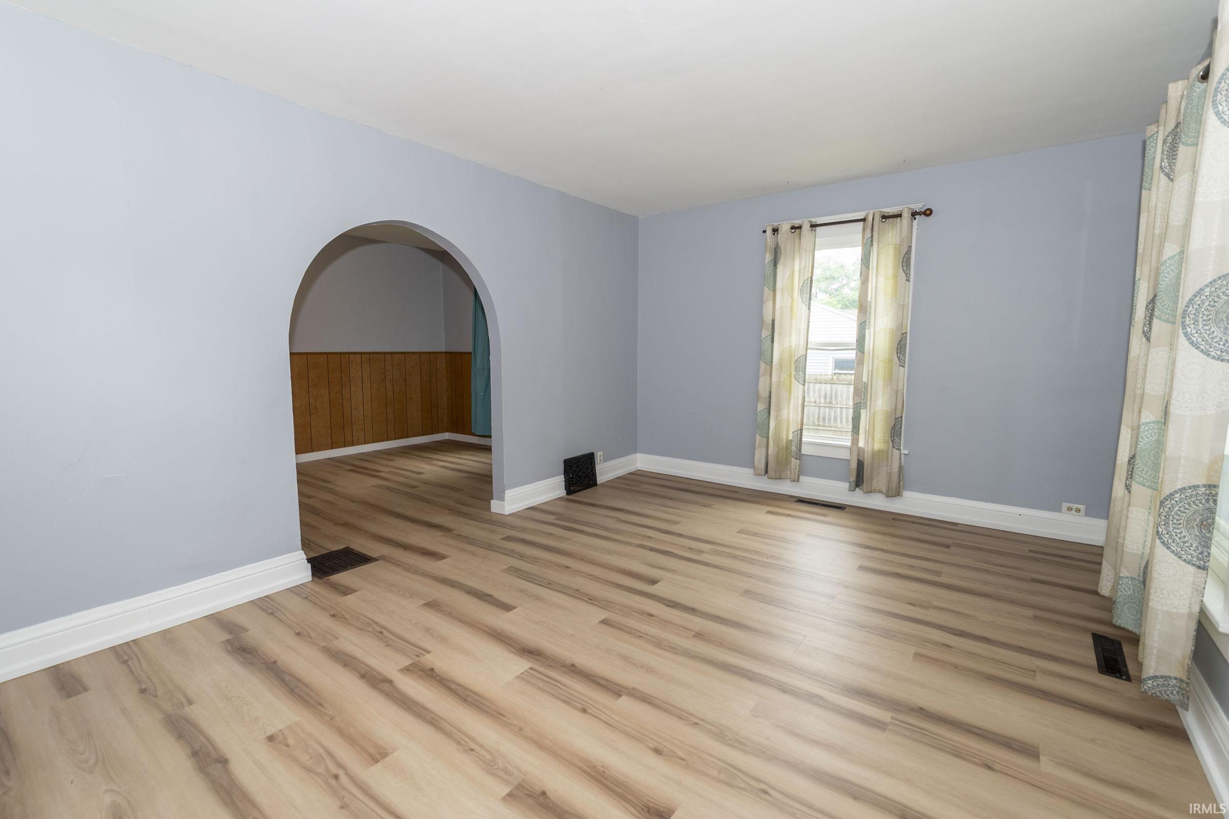 Bright room featuring wood-finish flooring, light blue wall paint, white baseboards, and a window with white trim