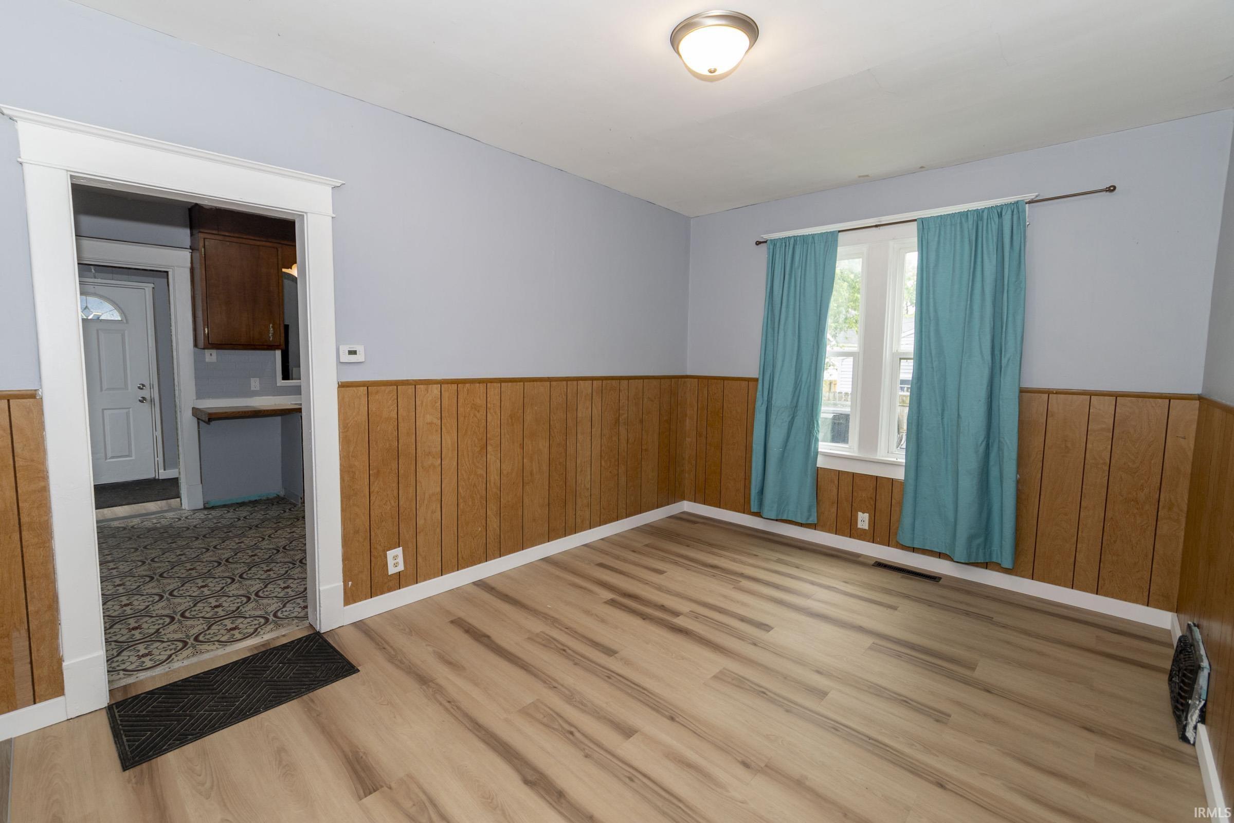 Spacious room featuring wood-finish flooring, half-wall paneling, and a neutral wall color
