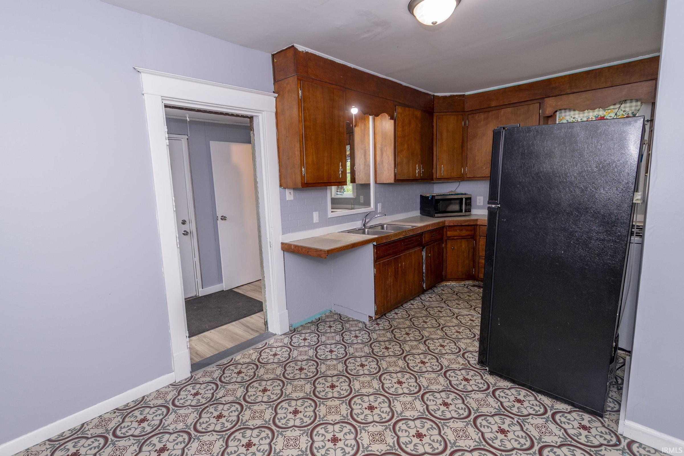 Kitchen featuring patterned floor tiles, wood cabinetry, light-toned countertops, and a stainless steel sink