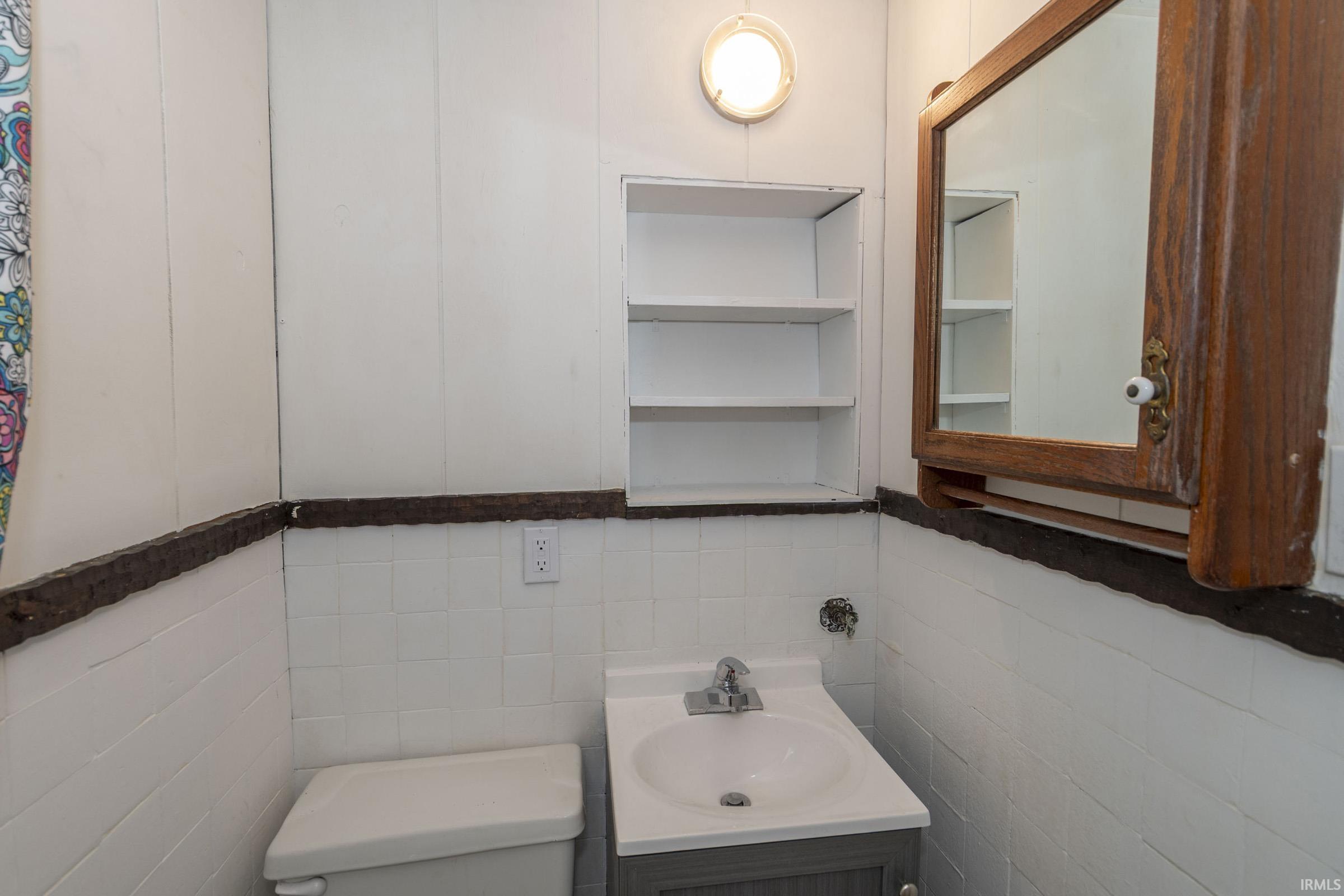 Bathroom featuring a wood-framed medicine cabinet, built-in shelving, a circular wall-mounted light fixture, and a white tiled half-wall