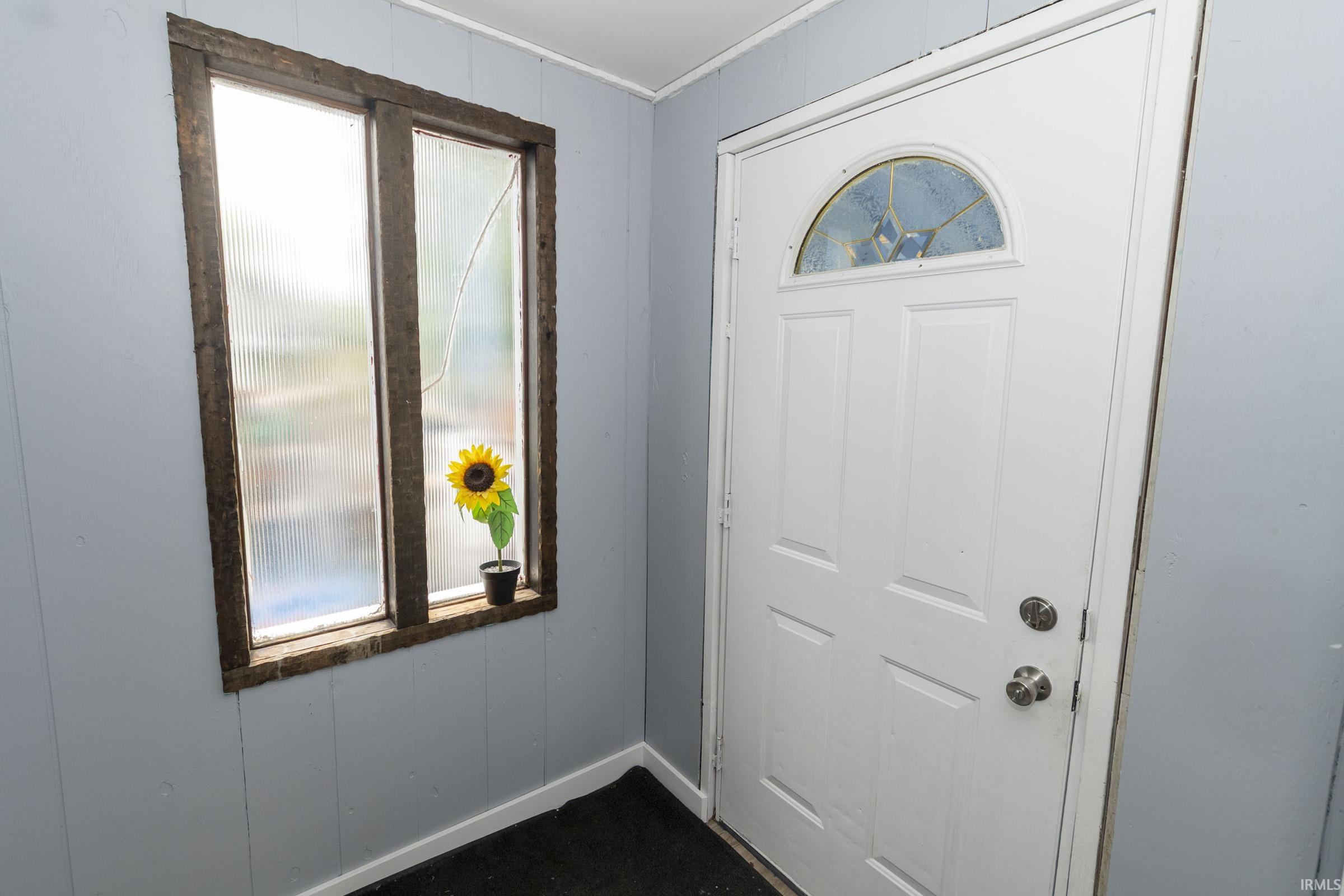 Entryway featuring a paneled white door with an arched decorative glass insert, a multi-pane window with wood framing, and light gray wall paneling